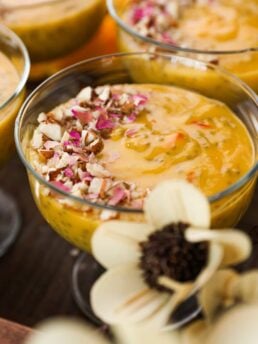 close up shot of a serving bowl with a thick orange coloured pudding garnished with nuts and dried roses.