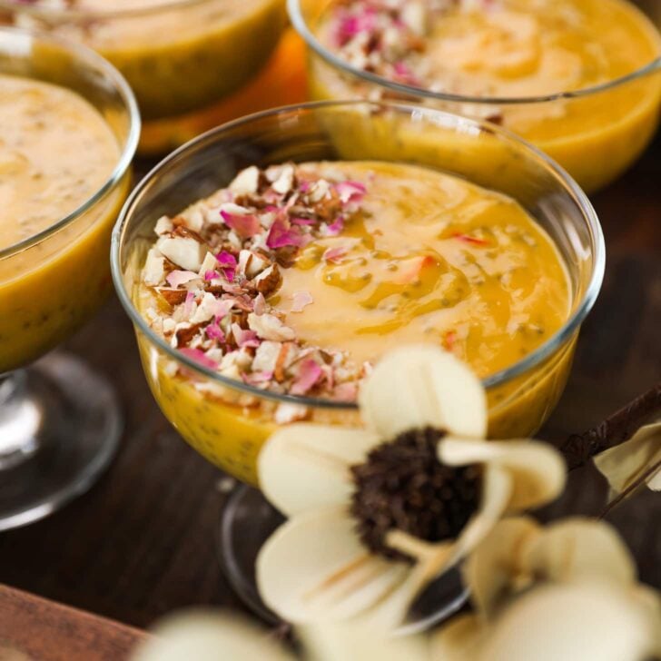 close up shot of a serving bowl with a thick orange coloured pudding garnished with nuts and dried roses.