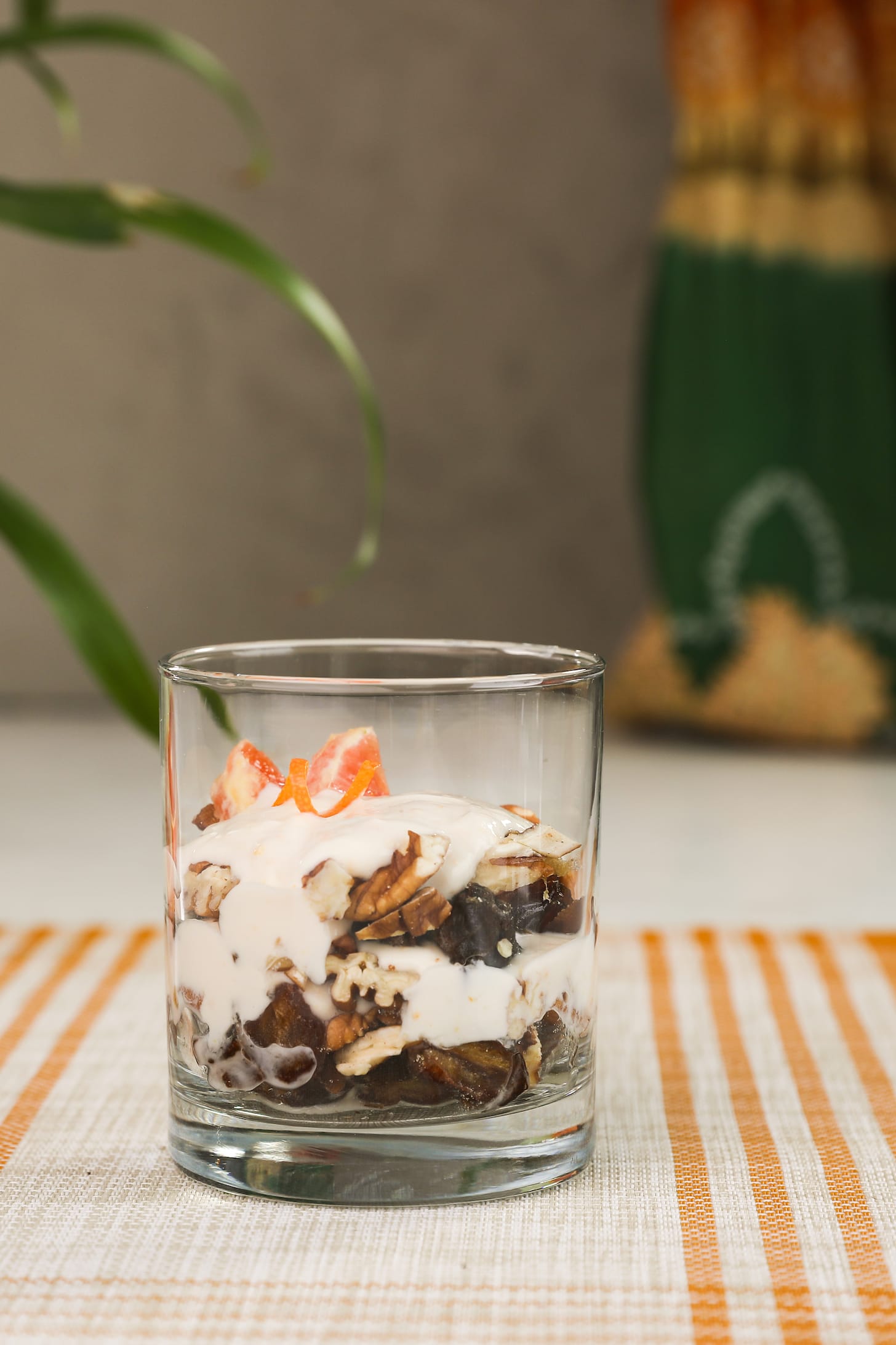 a glass filled with layers of yogurt and nuts with green leaves in the background.