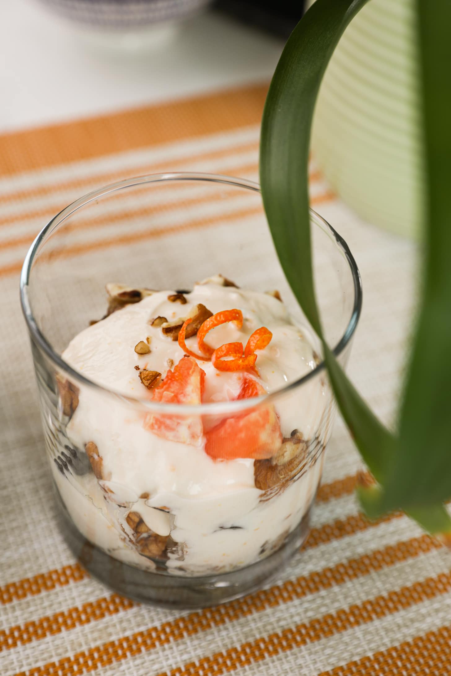 a glass filled with yogurt, topped with crushed nuts, orange rind curls and orange pieces.