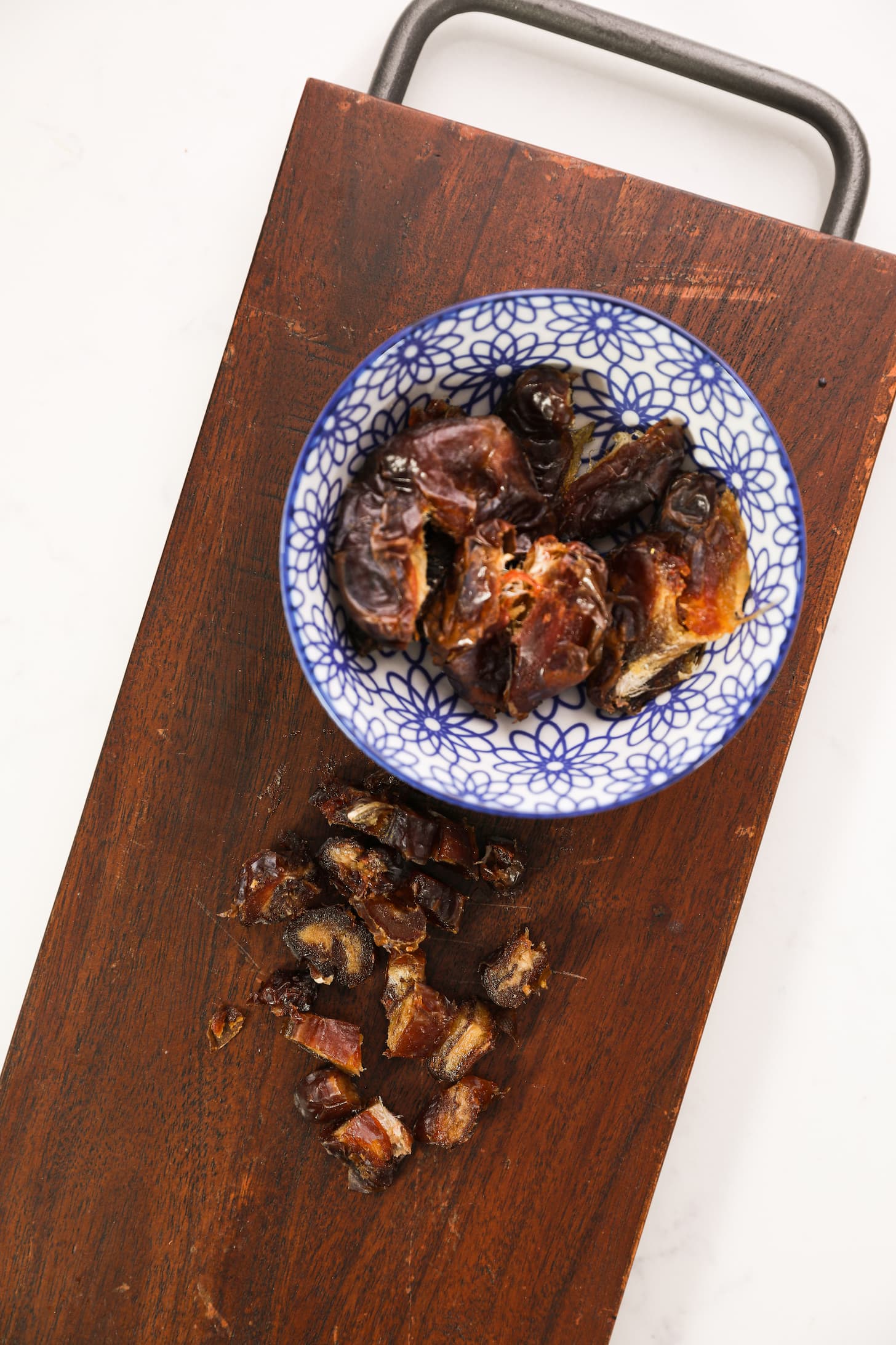 a bowl of pitted dates with chopped dates - both placed on a wooden rectangular board.