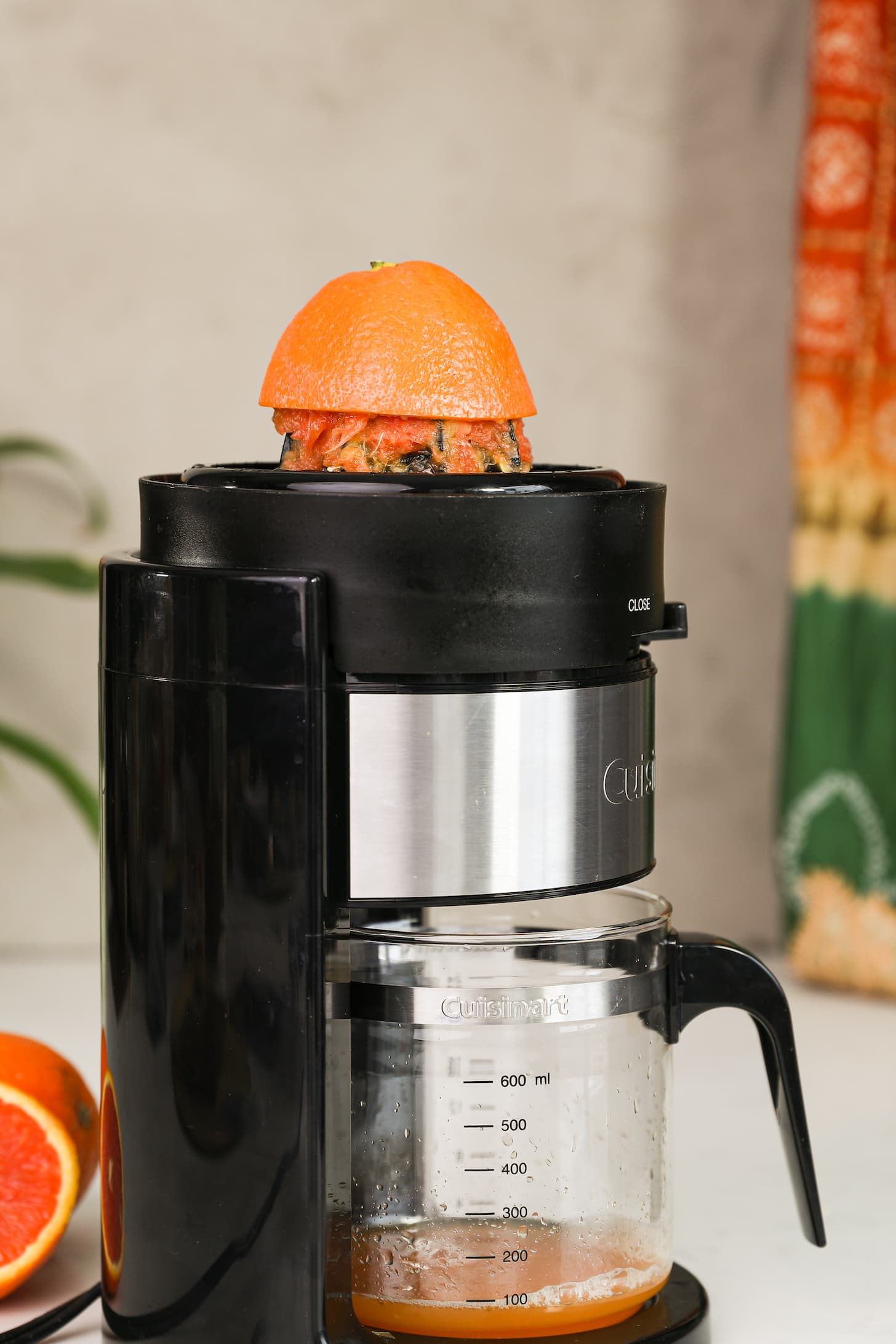 half an orange being juiced in a citrus juicer where the orange juice is collecting in a jug.