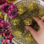 a hand grabbing a down nut covered ball on a gold printed plate with purple flowers on one side.