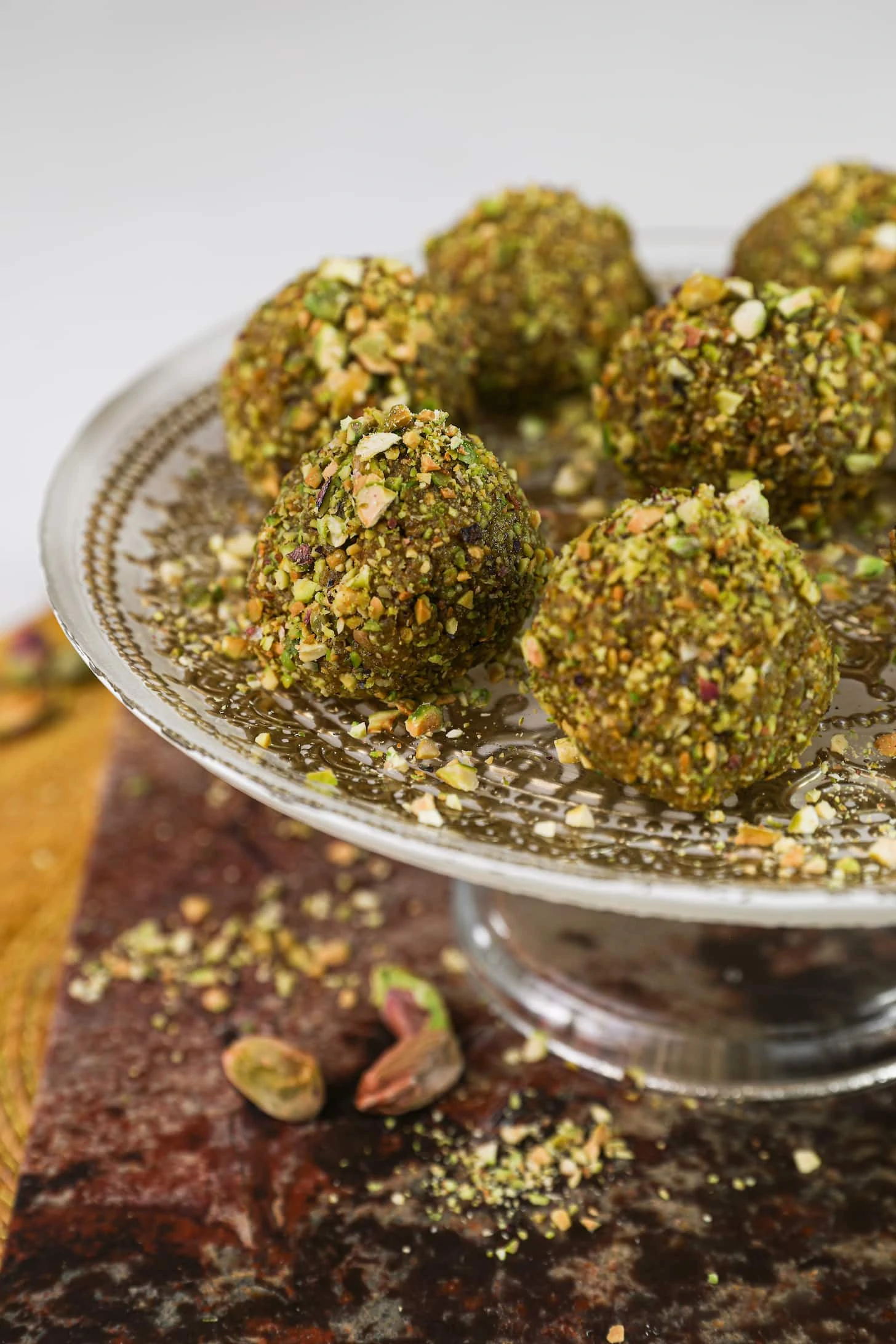 a close up shot of nut covered brown balls on a gold printed decorative cake holder.