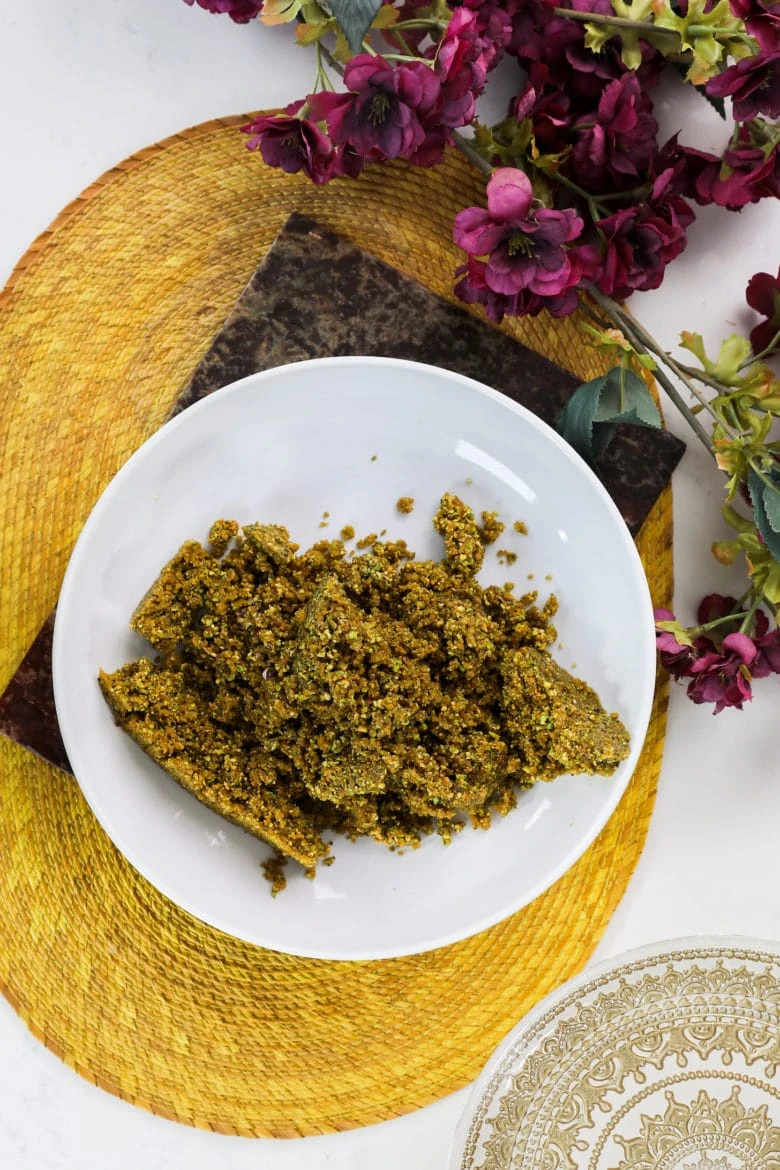 a bowl of a brown dough-like mixture of nuts and dried fruits on a yellow mat with flowers on one side.
