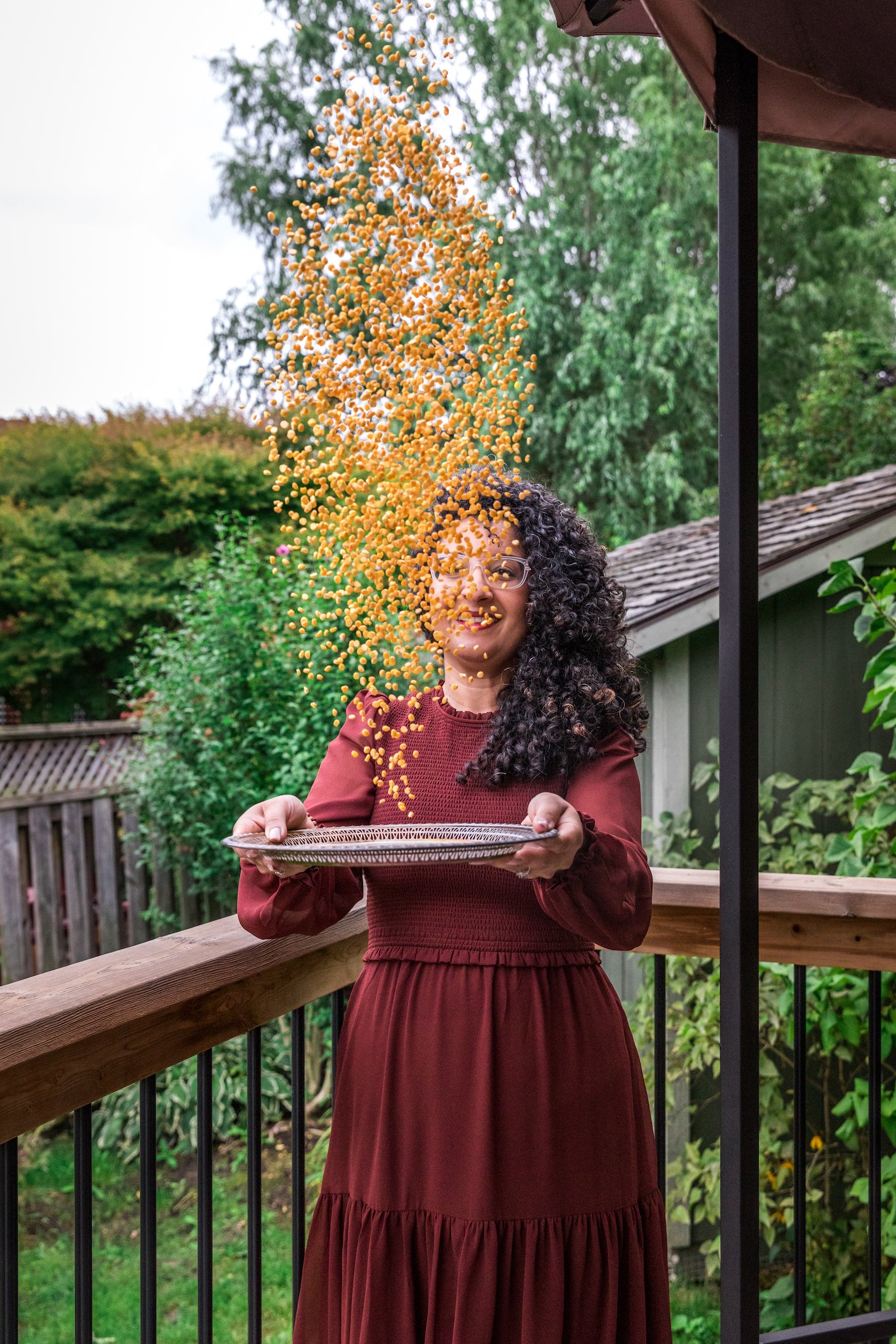 a lady on a deck in a garden throwing lentils up in the air from a tray. She looks happy.