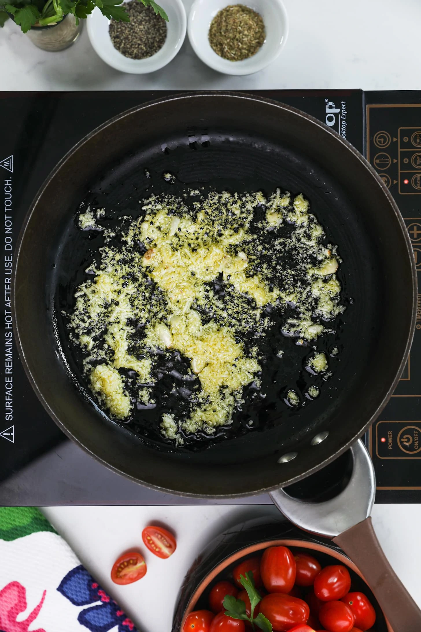 pan with crushed garlic frying in oil on top of a mobile cooktop.