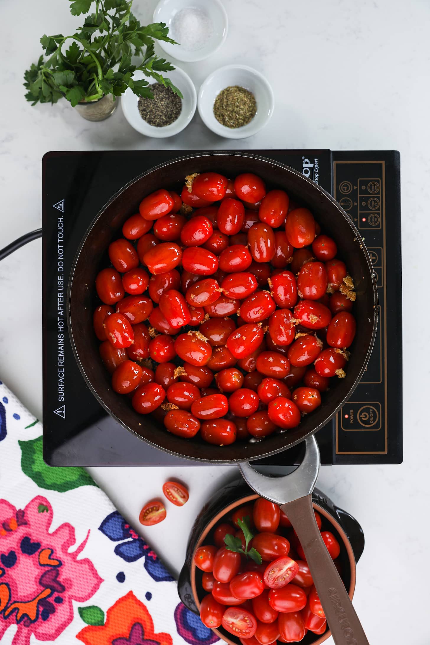 pan filled with baby red tomatoes on top of a mobile cooktop.