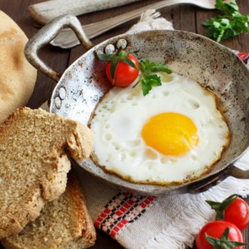Fried egg with tomatoes, homemade bread and herbs on a old frying pan on wood