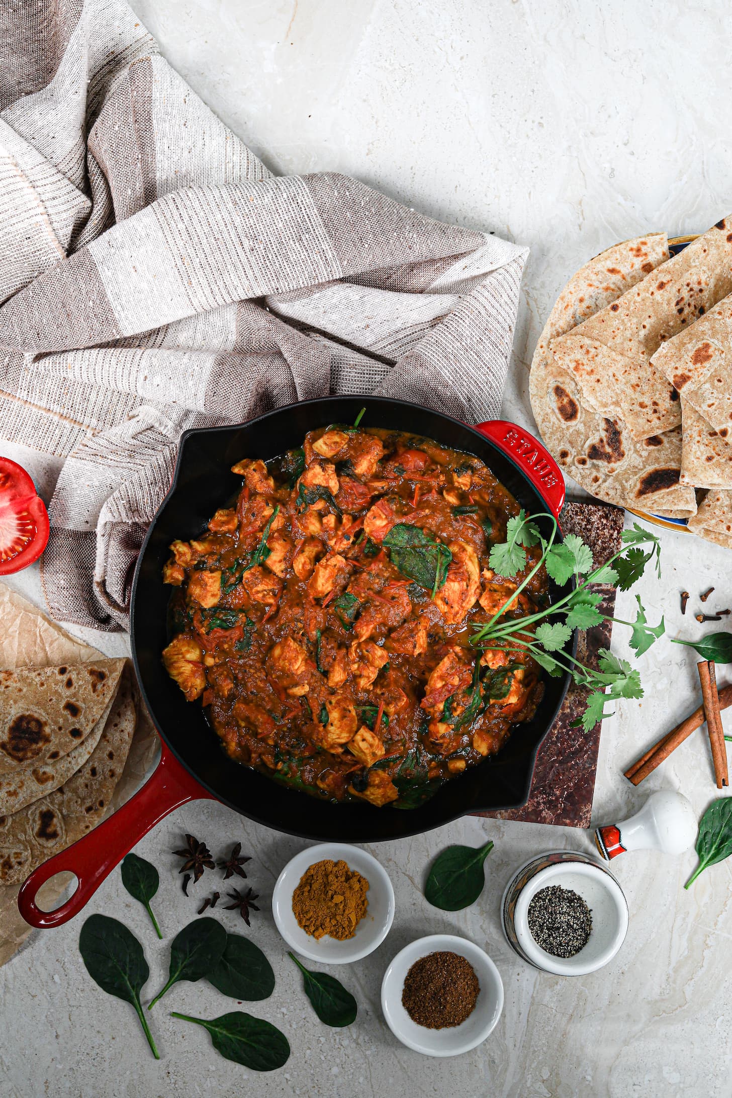 a red pan of chicken curry surrounded by roti (traditional Indian flatbread) and ramekins of spices.