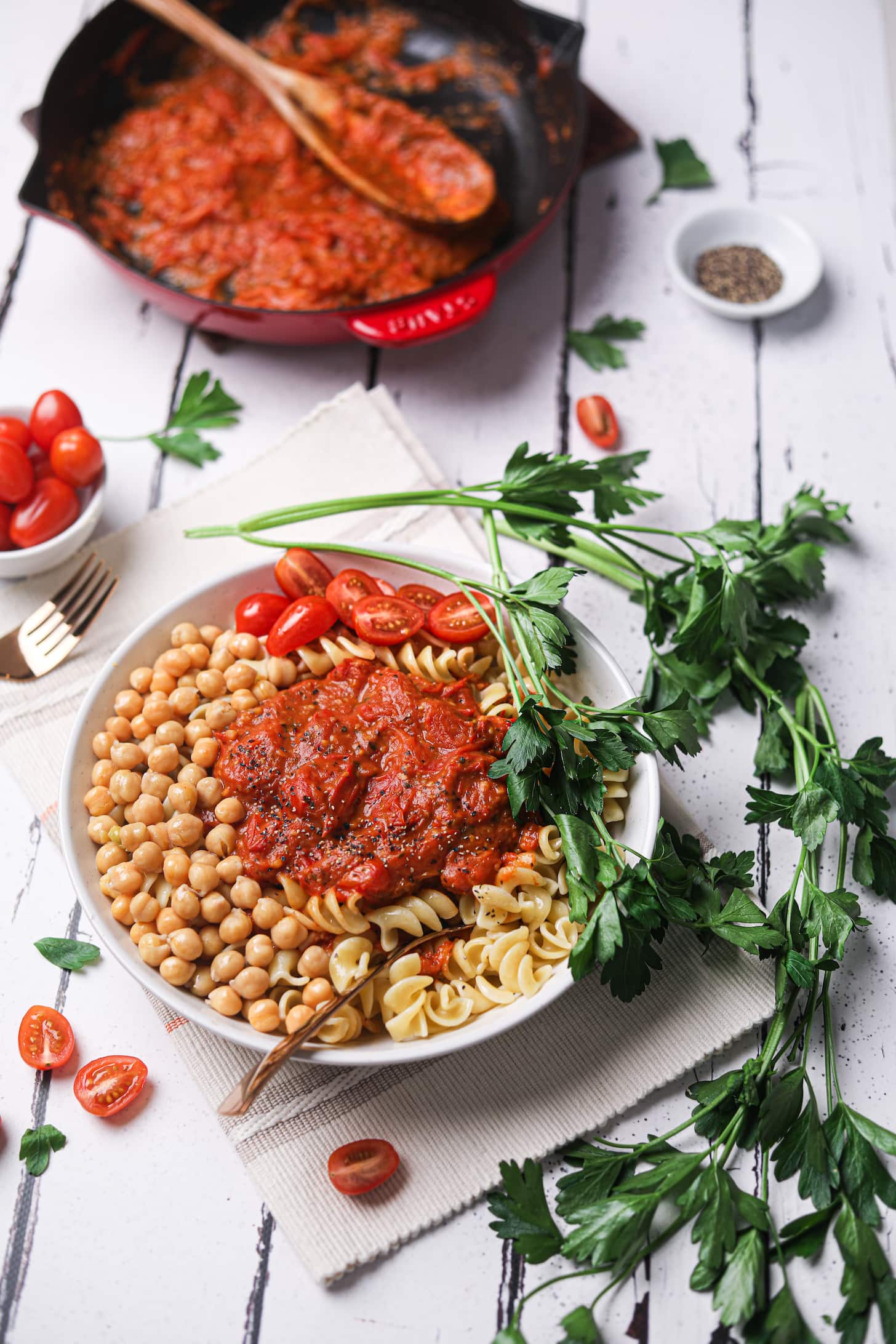 bowl of pasta and chickpeas topped with thick tomato sauce styled with stems of parsley.
