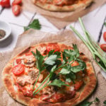 naan pizza topped with tomato sauce and chunks of canned salmon garnished with stems of fresh parsley.