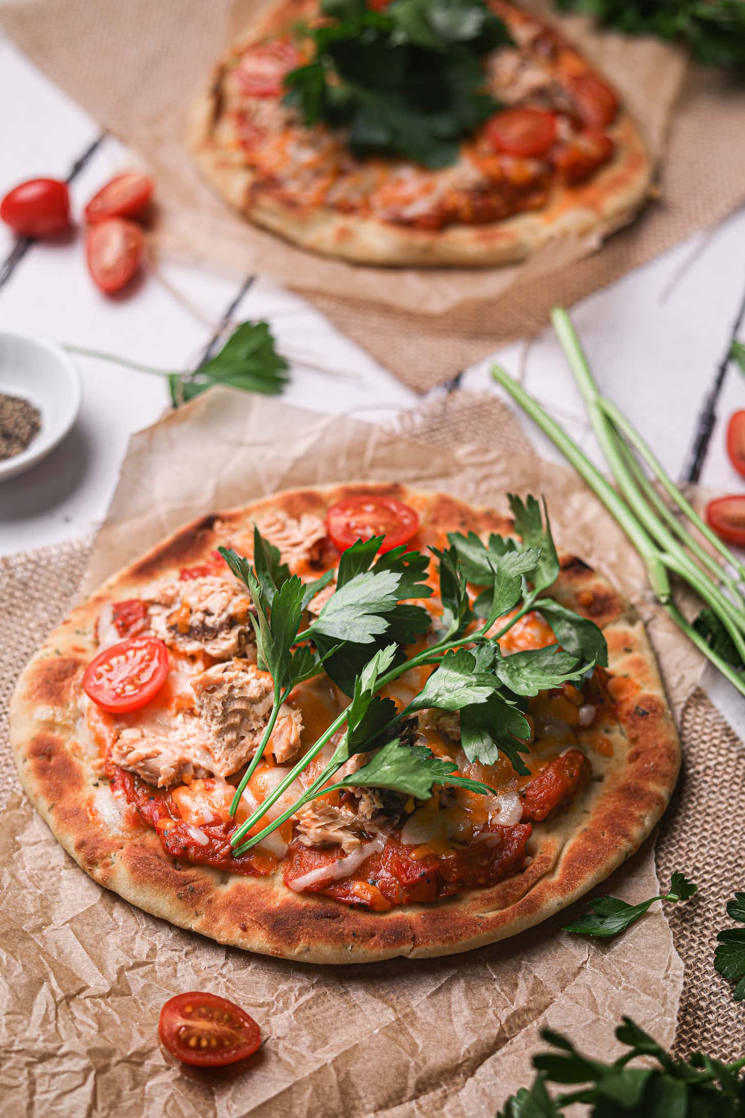 naan pizza topped with tomato sauce and chunks of canned salmon garnished with stems of fresh parsley.