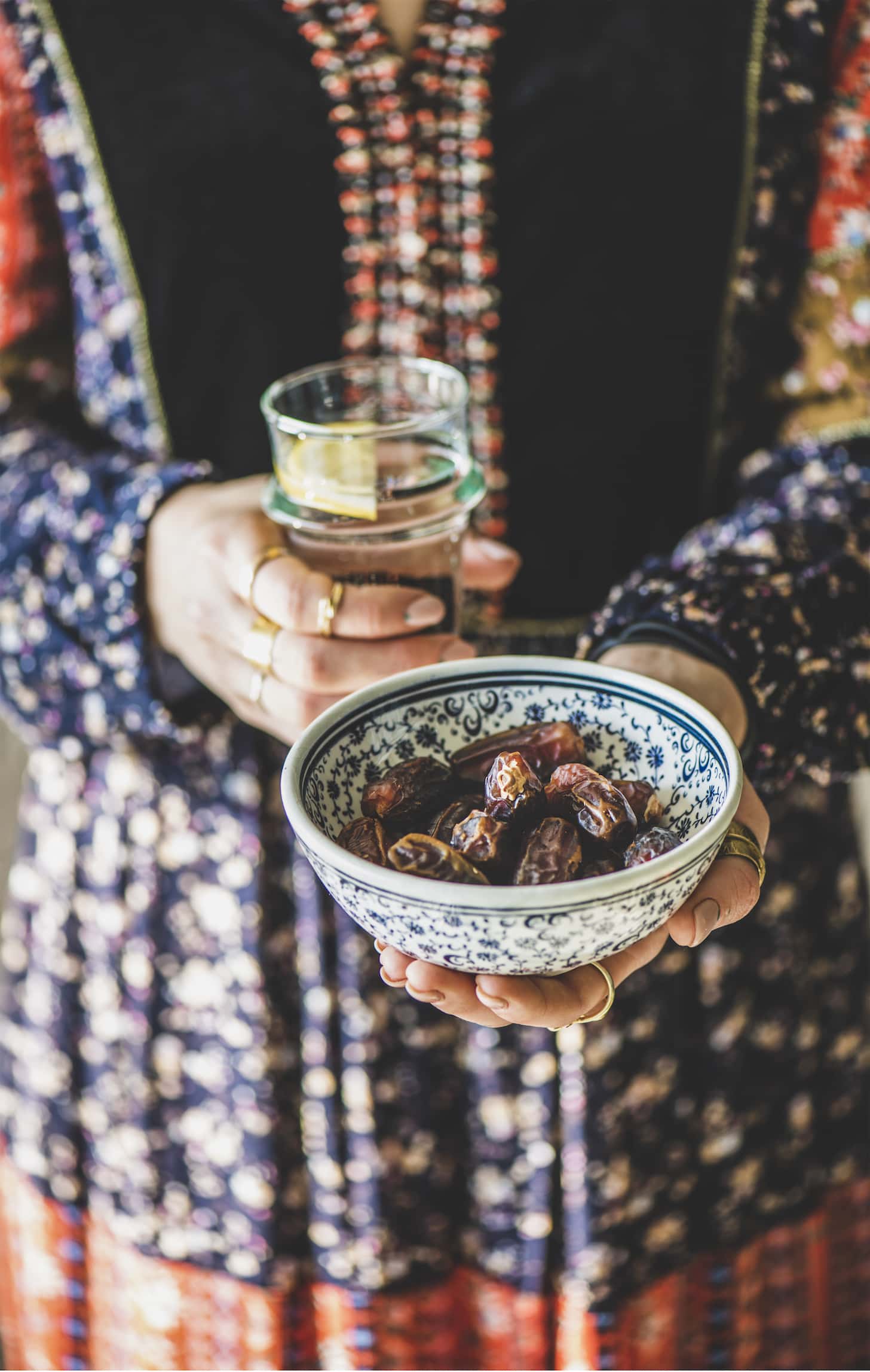 Woman in oriental dress holding bowl of dates and fresh drinking water in hands for Ramadan iftar evening meal and fasting month. Ramazan Muslim fasting food and islamic Middle East tradition