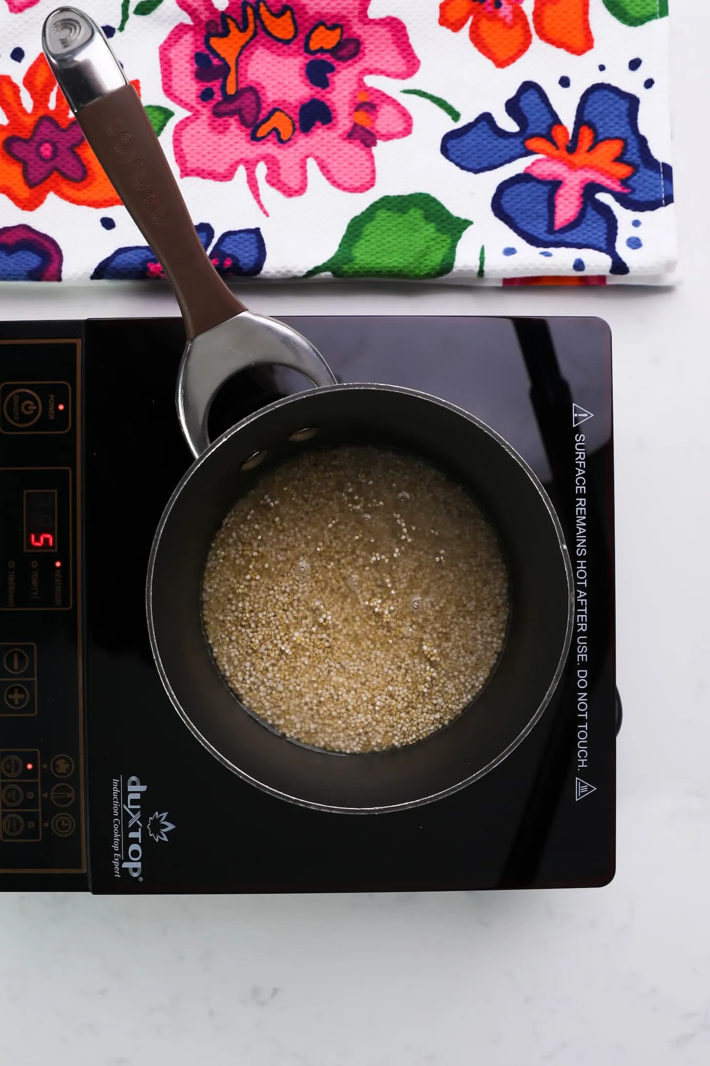 a saucepan with water and some grains on a mobile stovetop.
