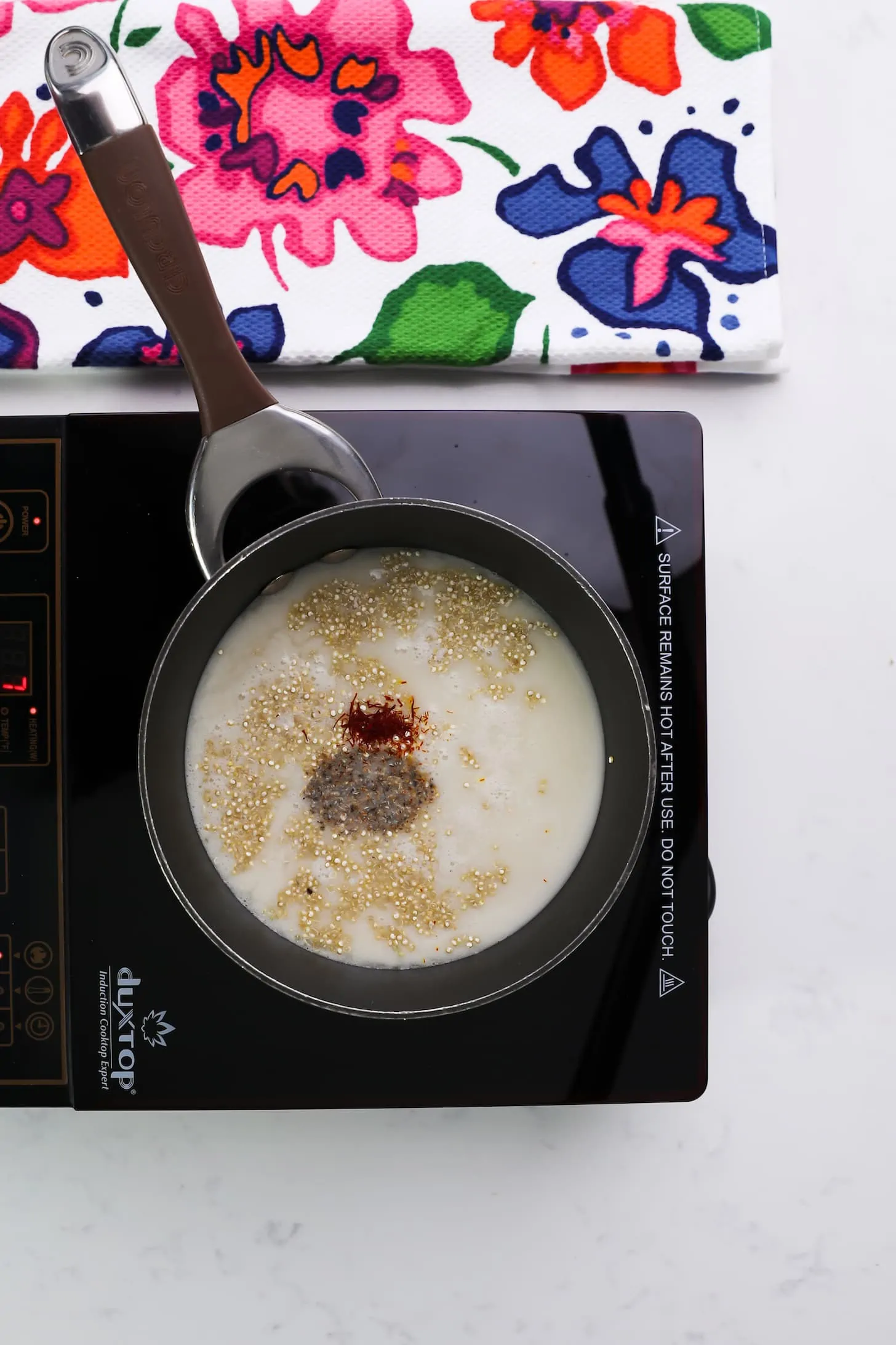 saucepan of milk with floating quinoa and two powdered ingredients on a mobile stovetop.