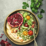 Rustic bowl with couscous salad with vegetables, hummus and fresh cut pomegranate. Middle eastern or Arab style meal with seasonings and fresh cilantro. Healthy Mediterranean dinner, toned image