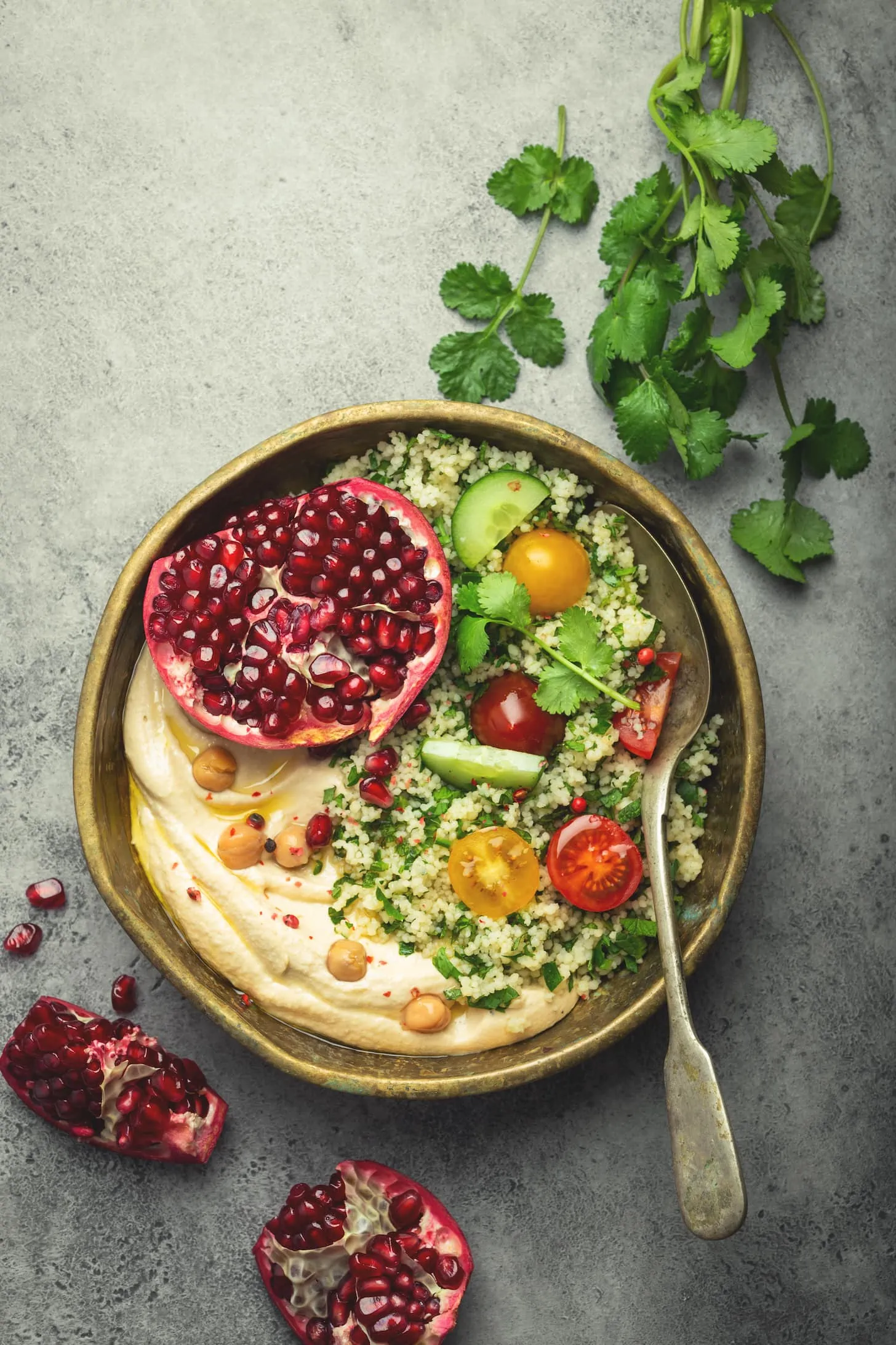 Rustic bowl with couscous salad with vegetables, hummus and fresh cut pomegranate. Middle eastern or Arab style meal with seasonings and fresh cilantro. Healthy Mediterranean dinner, toned image