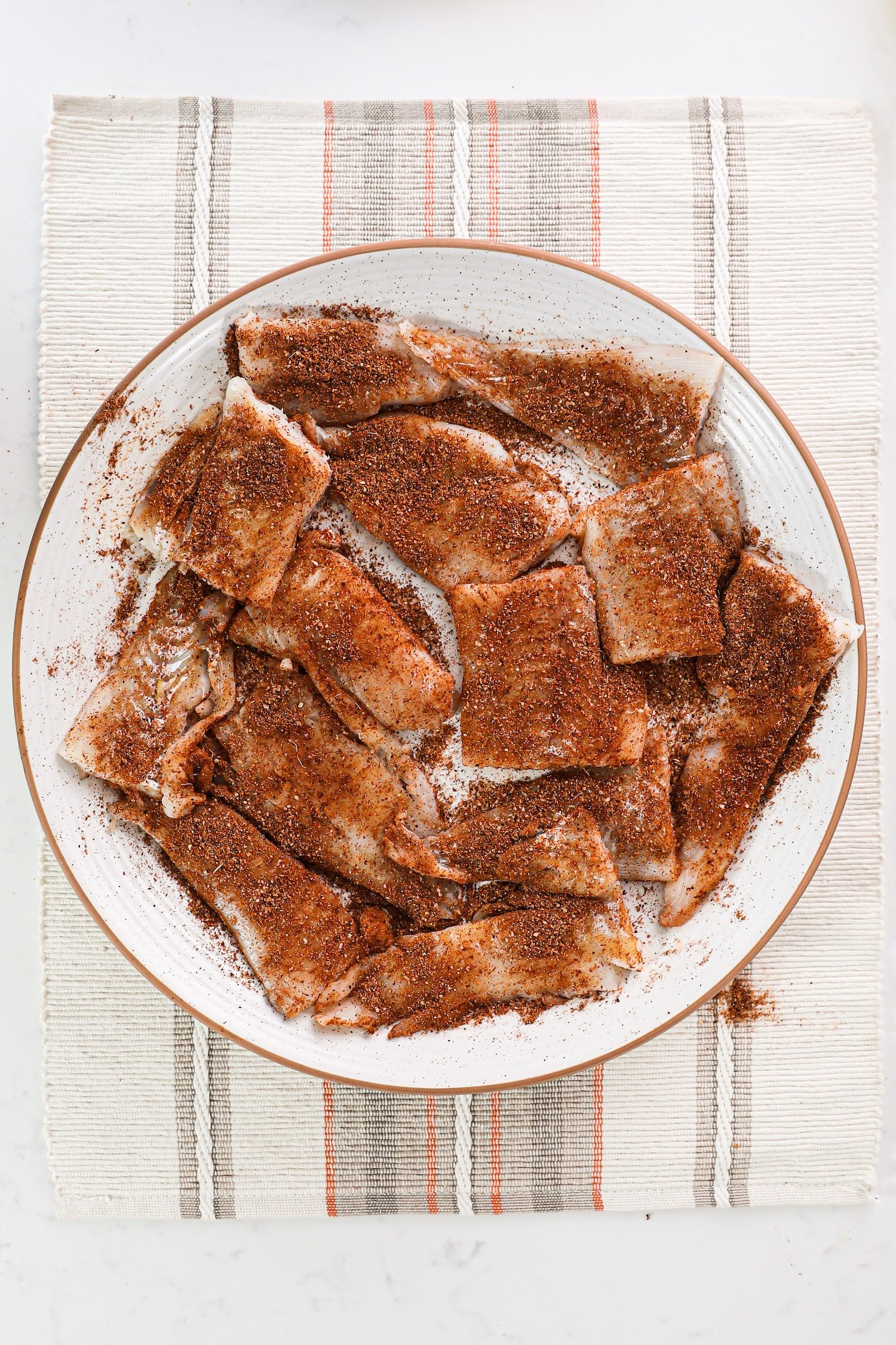 a plate of fish fillets coated in red spices arranged in a single layer.