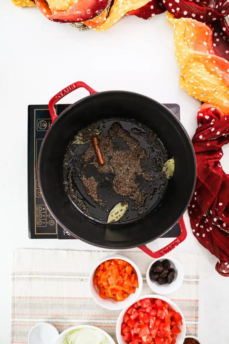 a large pot with cumin, cinnamon and bay leaves frying in it.