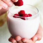 Girl holds glass of milk or yogurt, kefir with raspberries. Healthy and clean eating. Copy space. Breakfast, snack. Lifestyle concept
