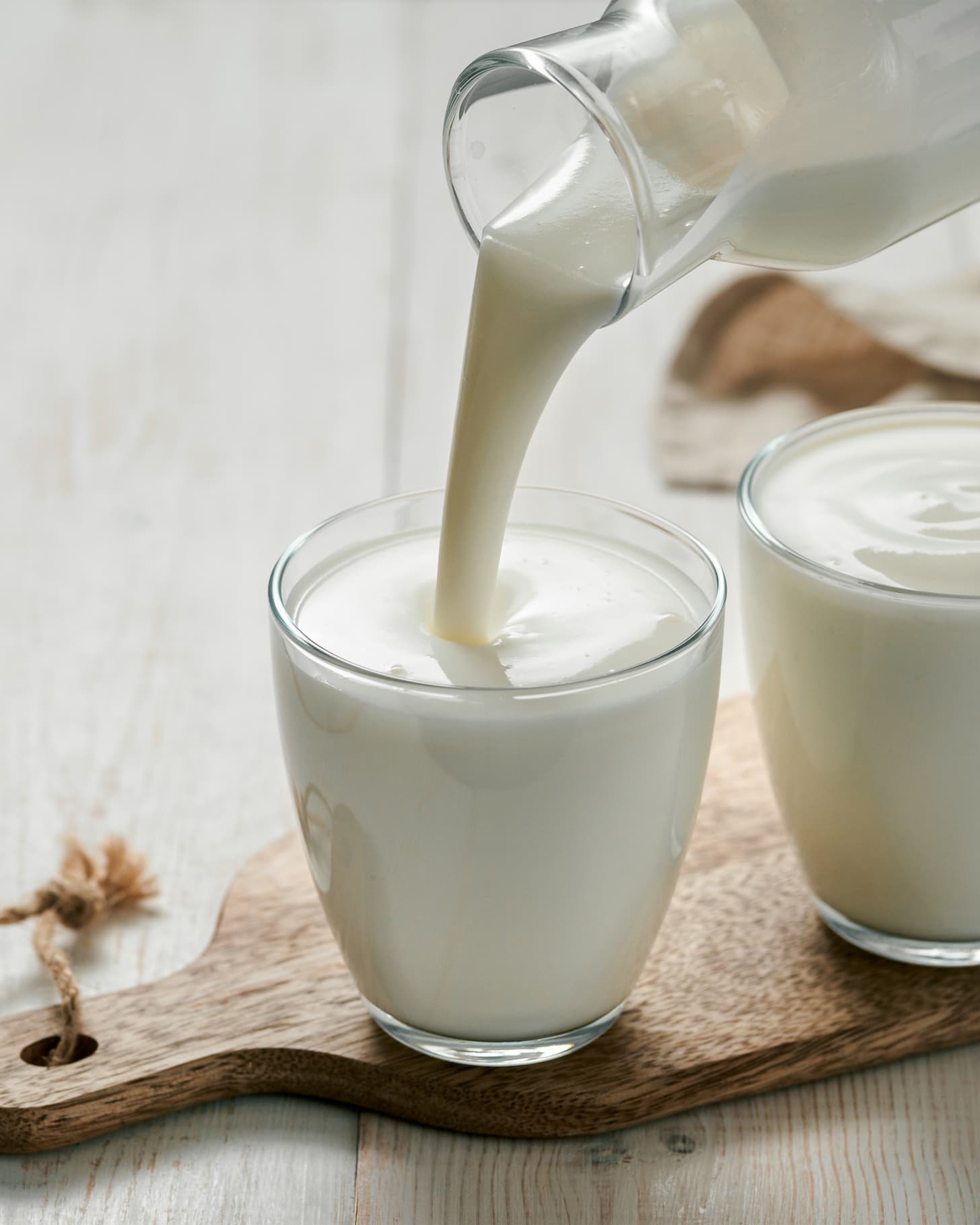 Pouring kefir, buttermilk or yogurt with probiotics. Yogurt flowing from glass bottle on white wooden background. Probiotic cold fermented dairy milk drink. Vertical