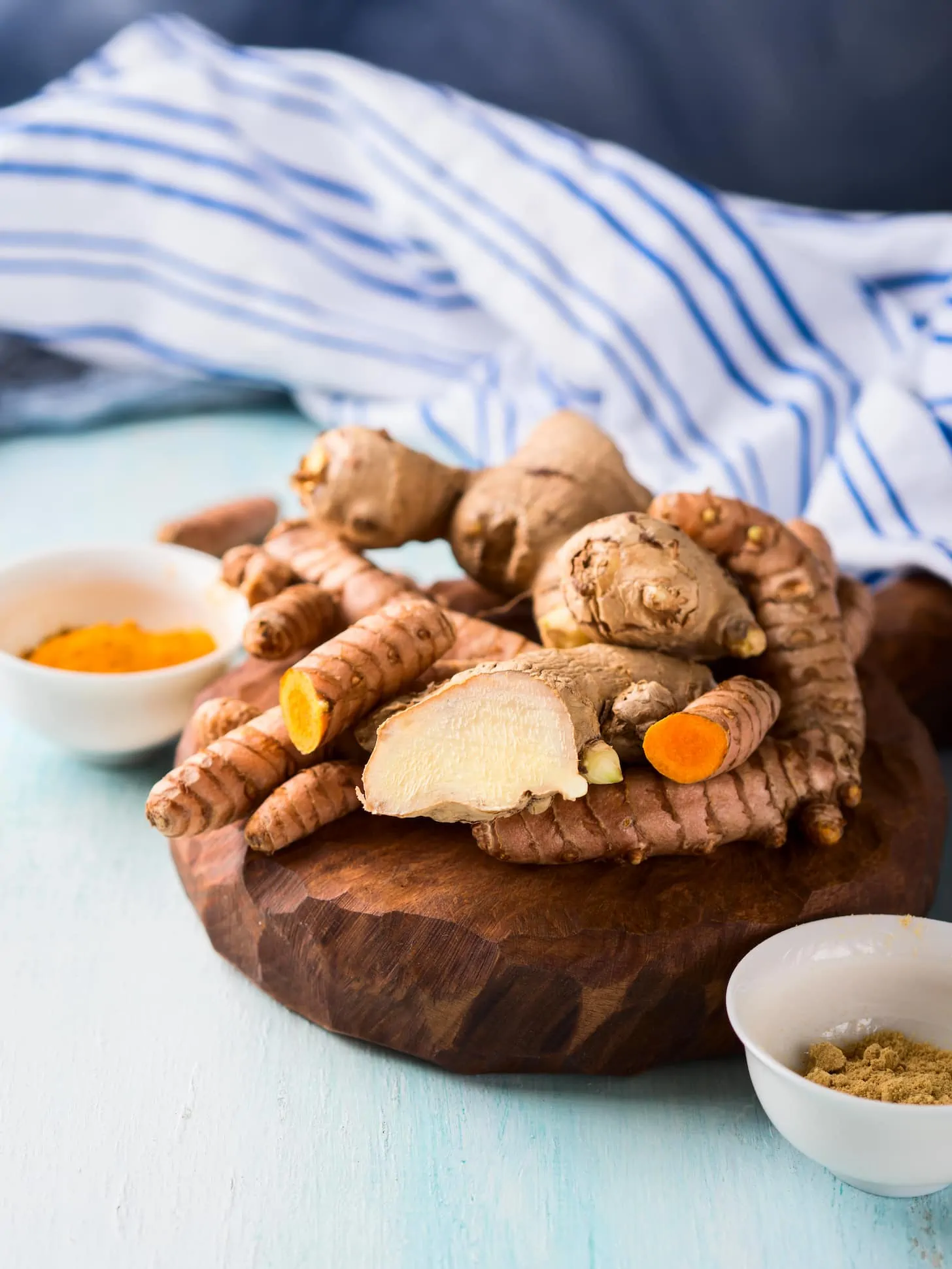 Turmeric spice and ginger in powder and roots on wooden board over blue background. Natural healthy remedy