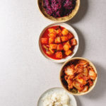 Variety of fermented food korean traditional kimchi cabbage and radish salad, white and red sauerkraut in ceramic plates over grey spotted background. Flat lay, space