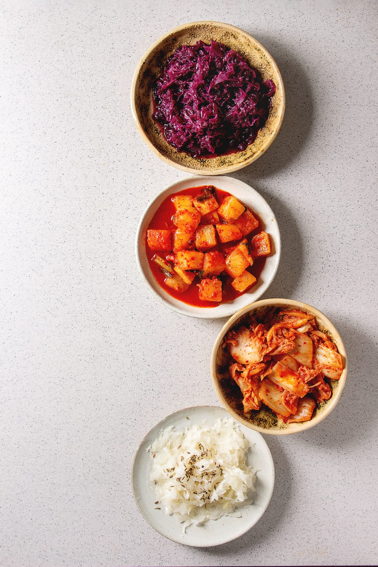 Variety of fermented food korean traditional kimchi cabbage and radish salad, white and red sauerkraut in ceramic plates over grey spotted background. Flat lay, space