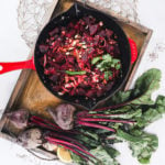 a pan of cooked cubes of beetroot topped with chopped almonds in a gold tray with raw whole beets on the side.