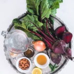 a silver round tray with a bunch of raw beets and other ingredients in ramekins including almonds, orange liquid and spice.