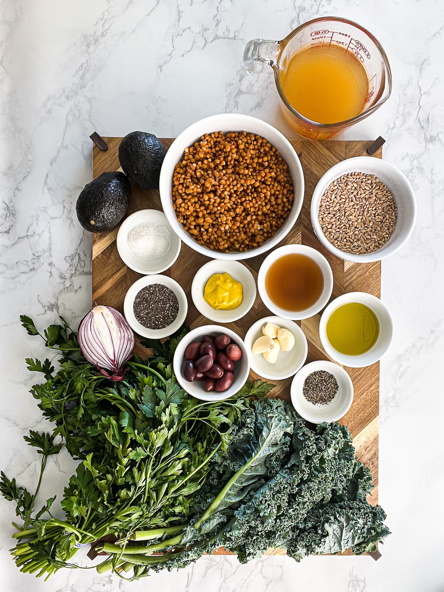 a variety of food ingredients - such as greens, lentils and herbs - beautifully arranged on a wooden board.
