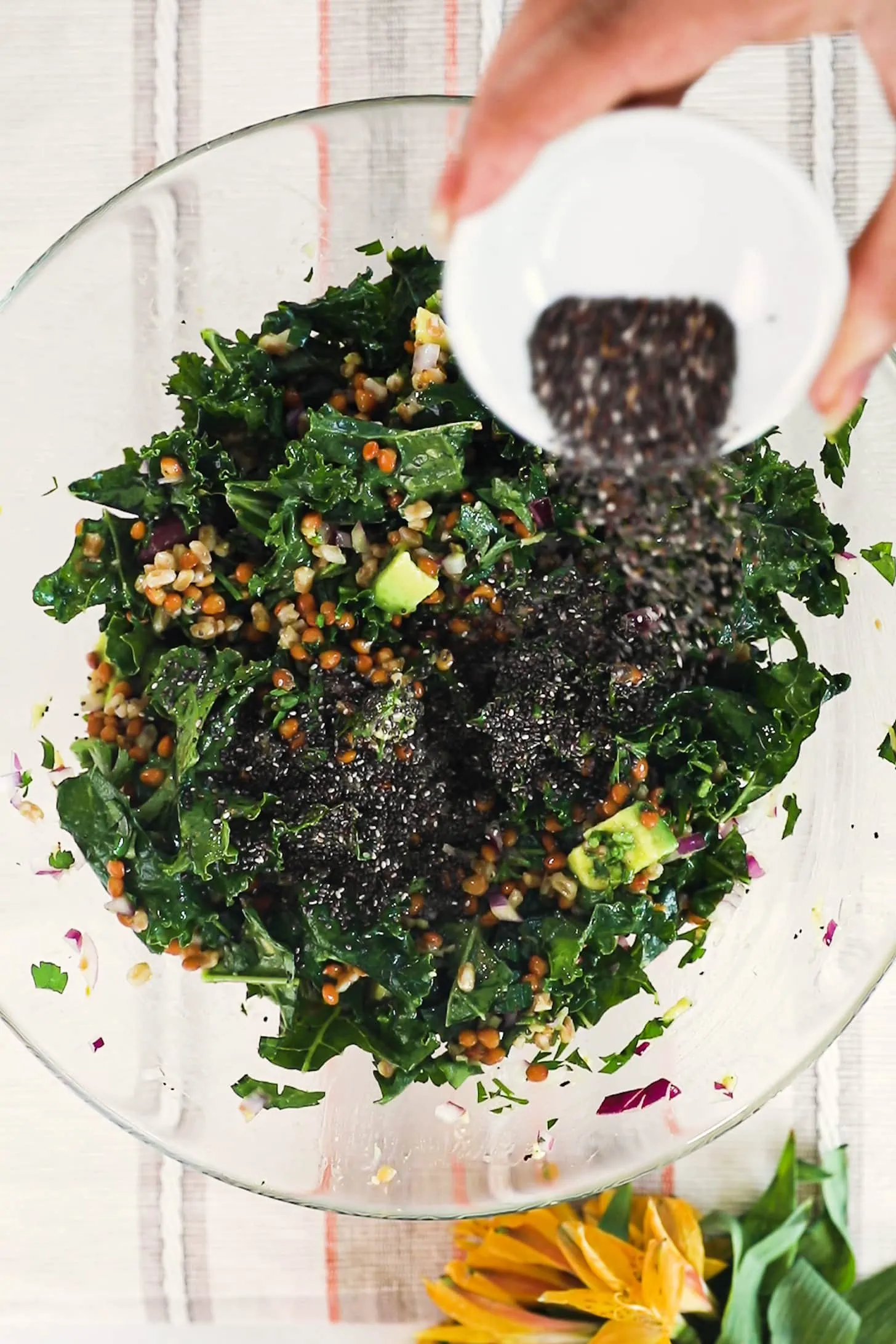 a hand sprinkling chia seeds over a bowl of salad.