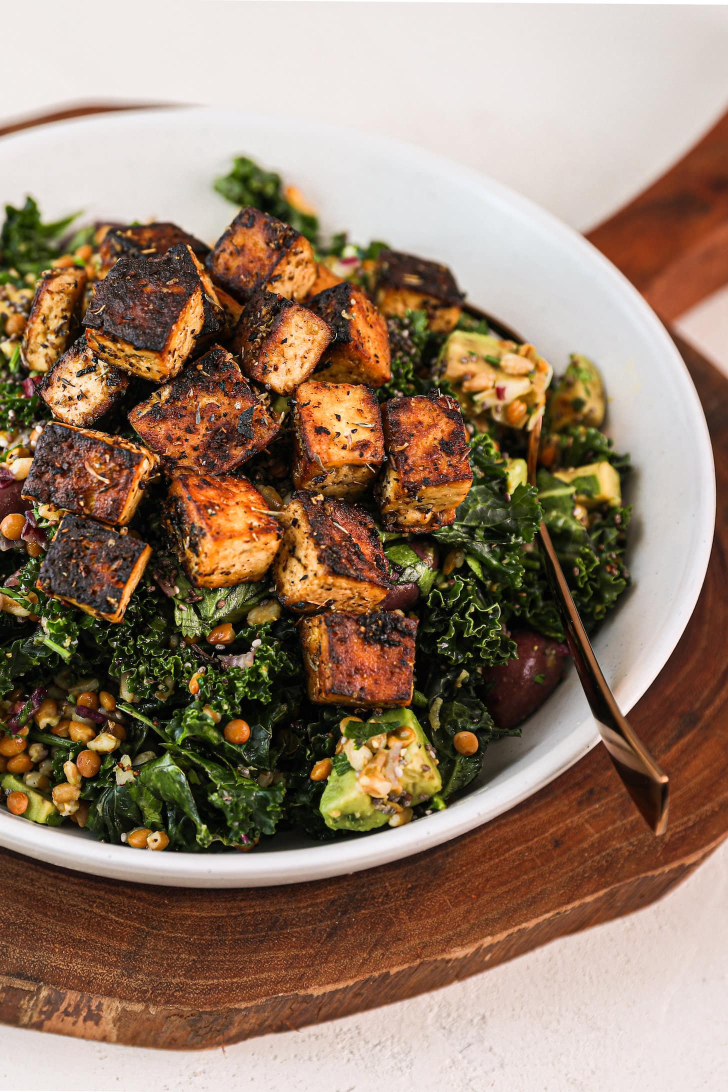 side shot bowl of a green grain salad topped with charred tofu cubes.