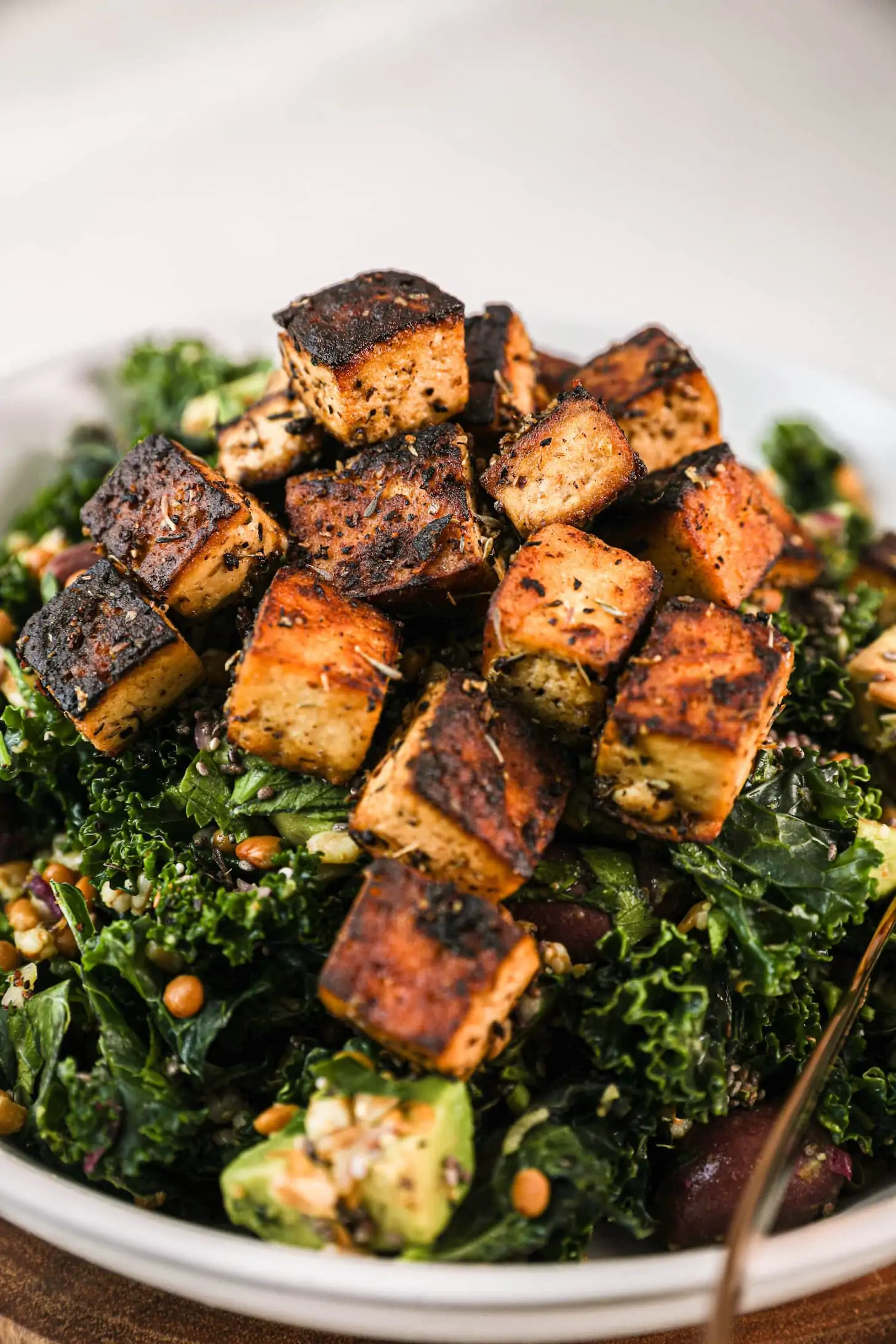 close up shot of a bowl of green grain salad topped with charred tofu cubes.