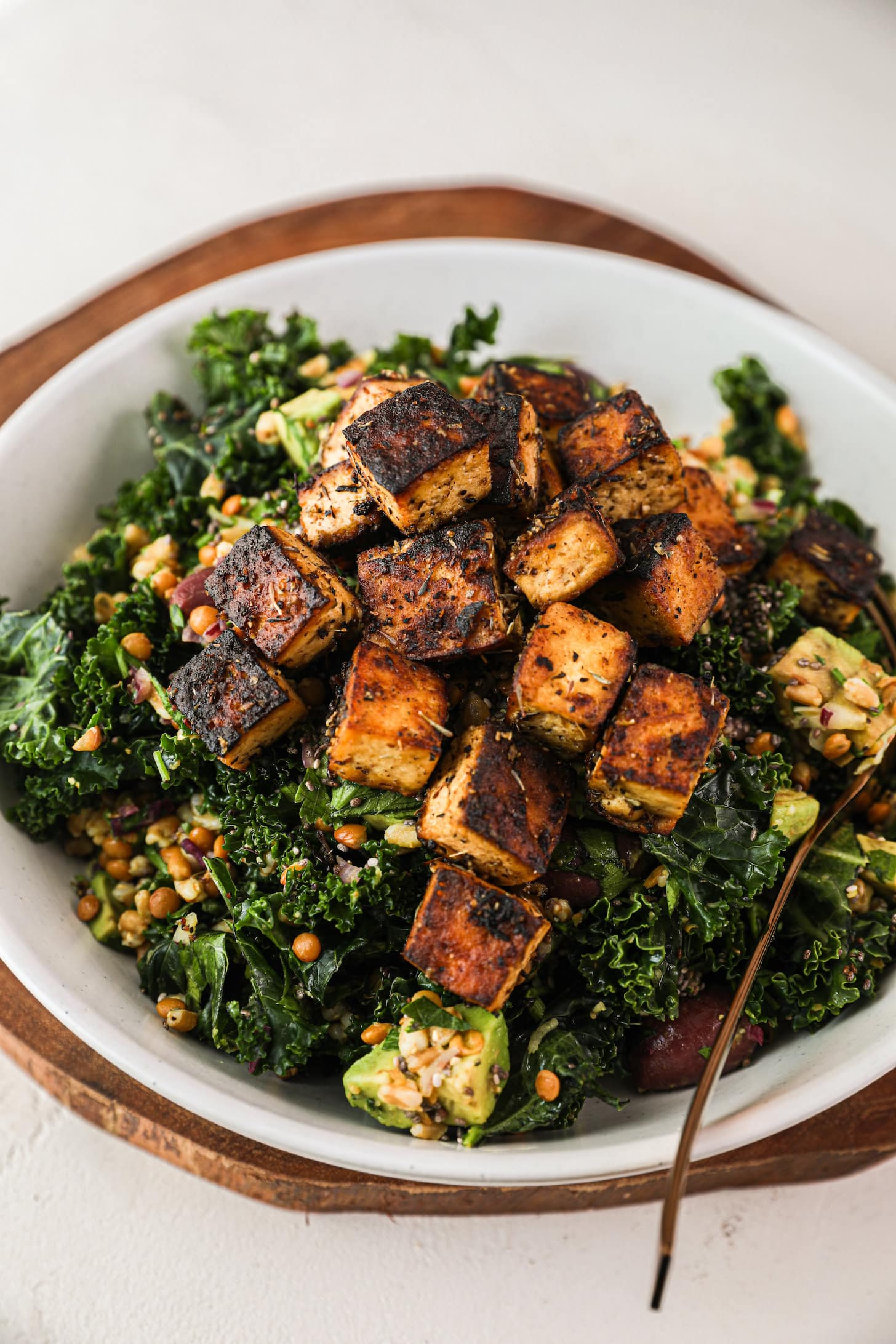 bowl of green grain salad topped with charred tofu cubes.