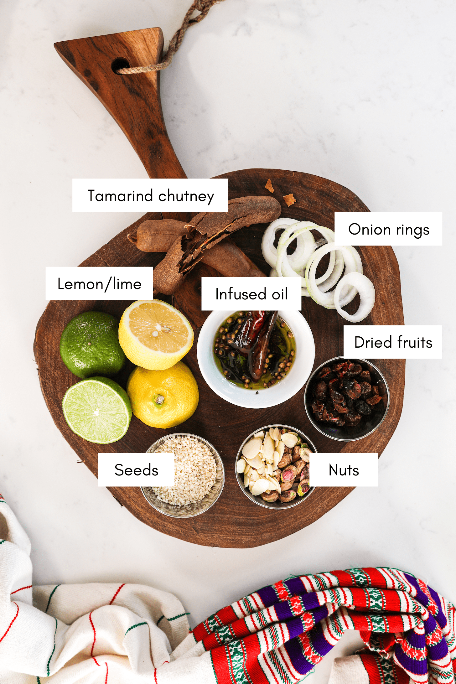 a wooden board with a plate of aromatics including onion, garlic, ginger and tamarind in different forms.