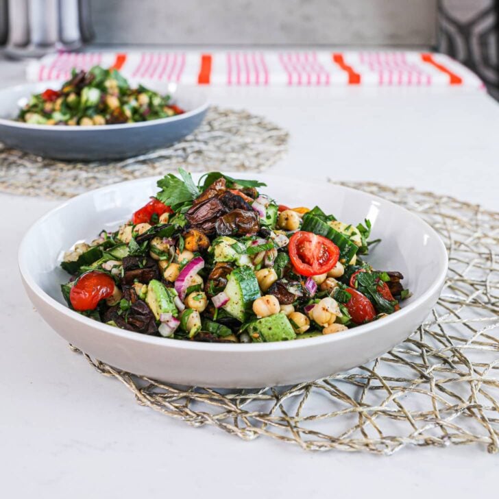 close up image of a bowl of salad made of chickpeas, cucumbers, tomatoes and herbs.