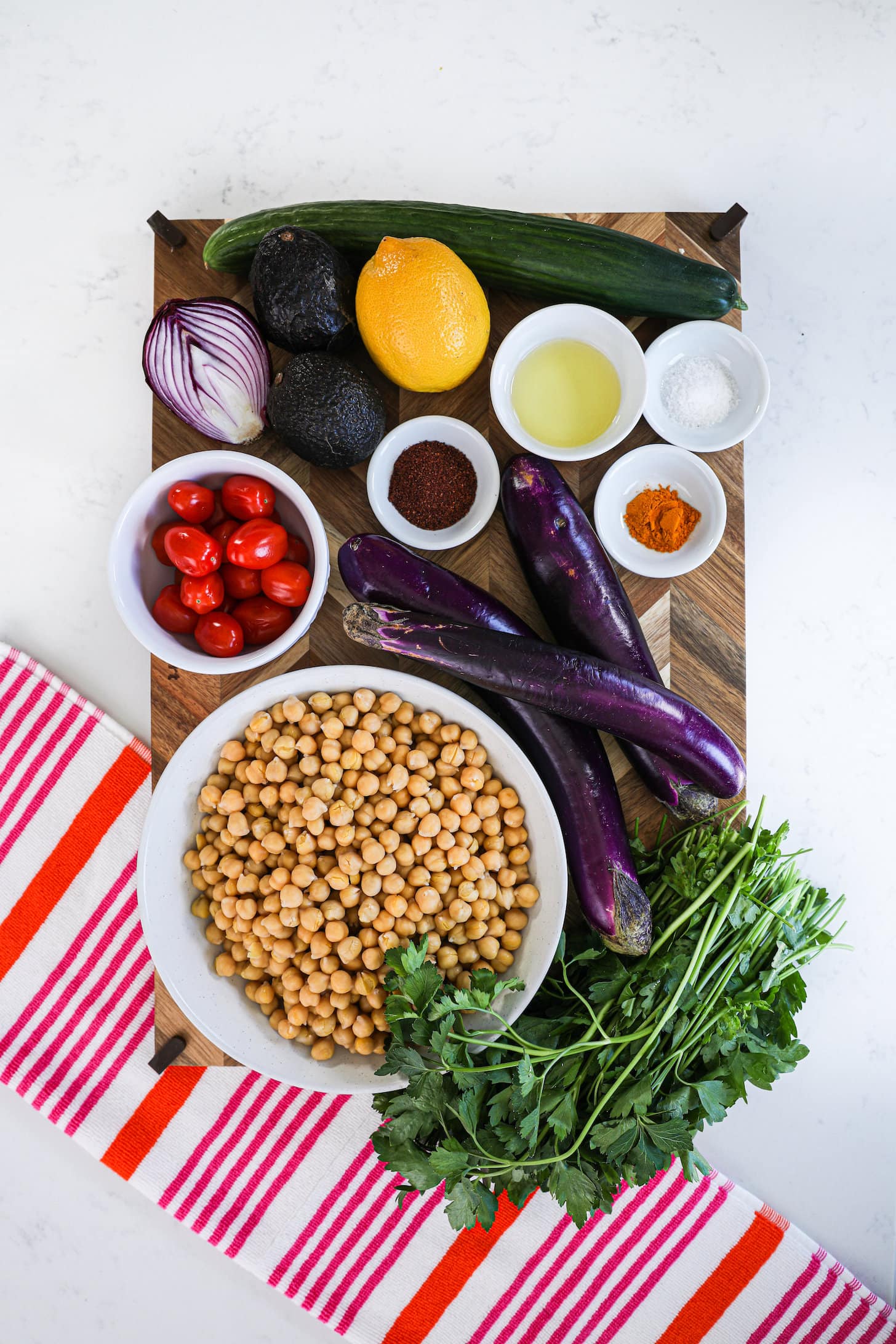 food ingredients on a wooden board including chickpeas, eggplants, tomatoes and spices.
