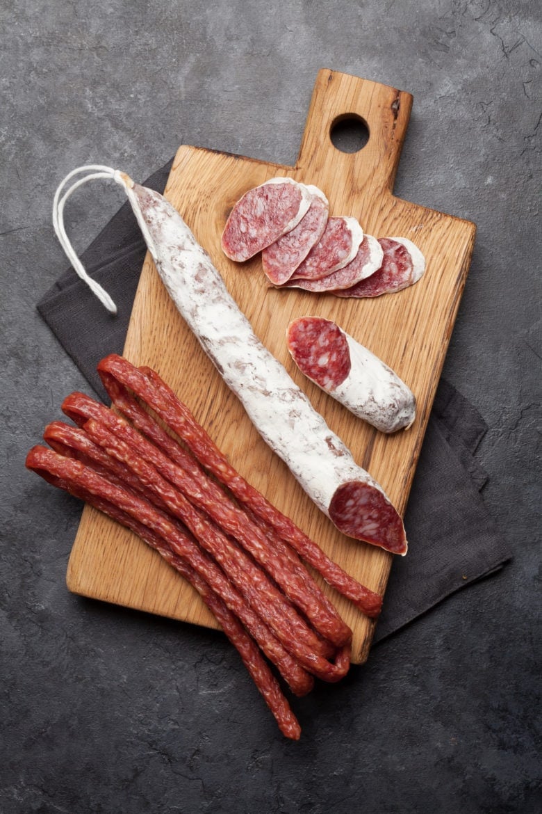 Snacks on cutting board over stone background. Sliced salami and sausages. Top view