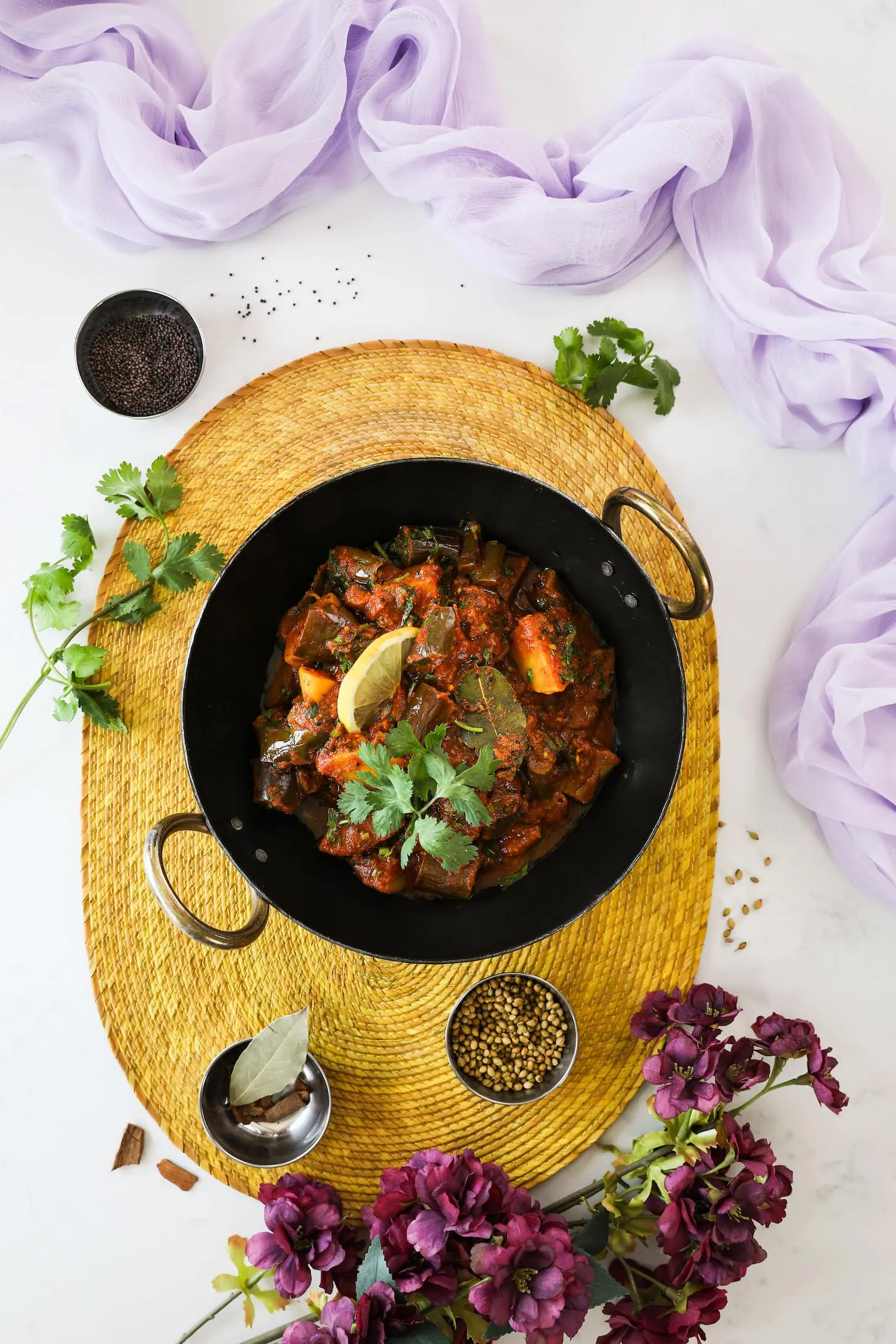 wok of cooked vegetables topped with a lemon slice and cilantro leaves on a yellow place mat styled with a lilac scarf and flowers