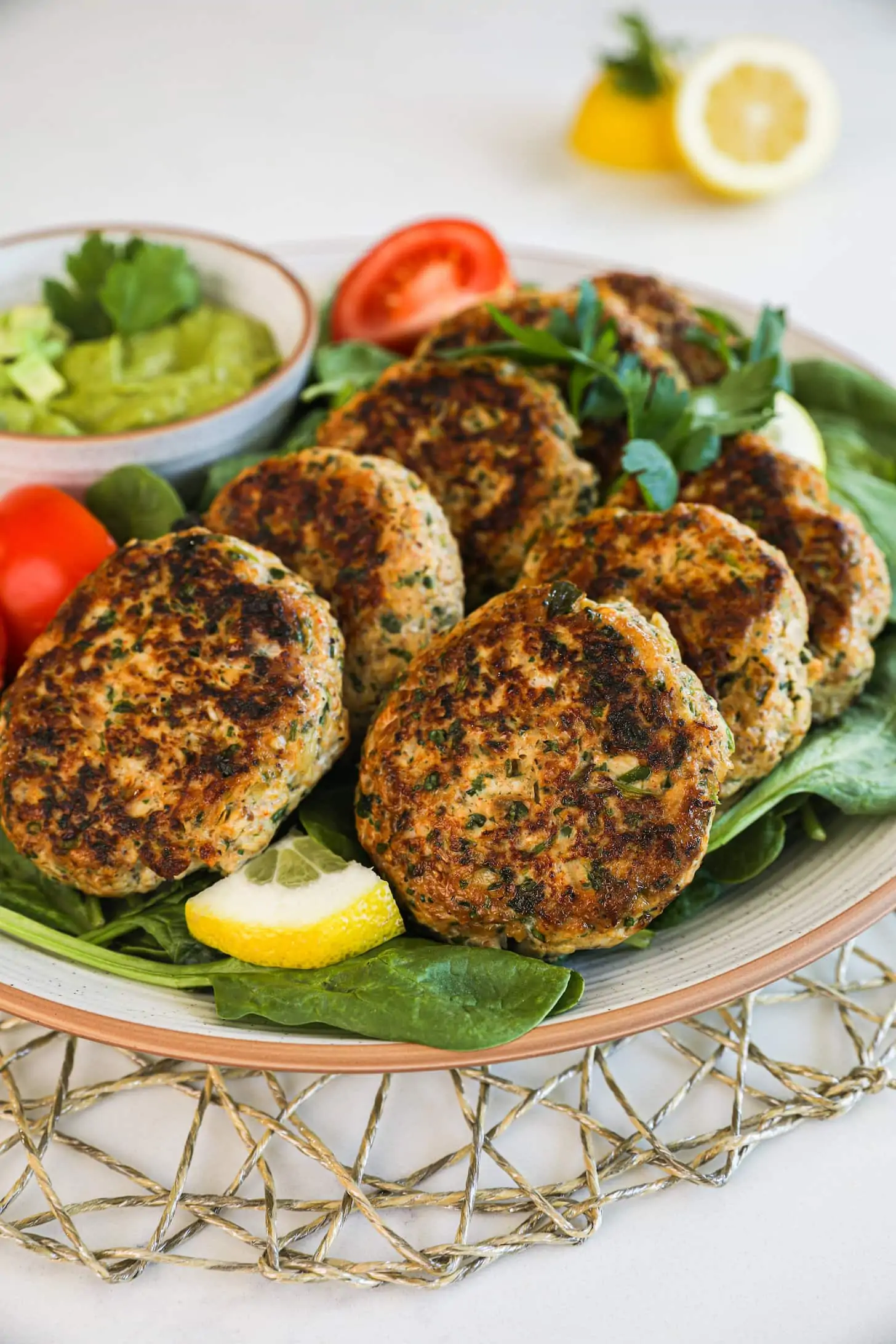 cooked patties overlaid on one another on a bed of greens with a bowl of dip on the side.