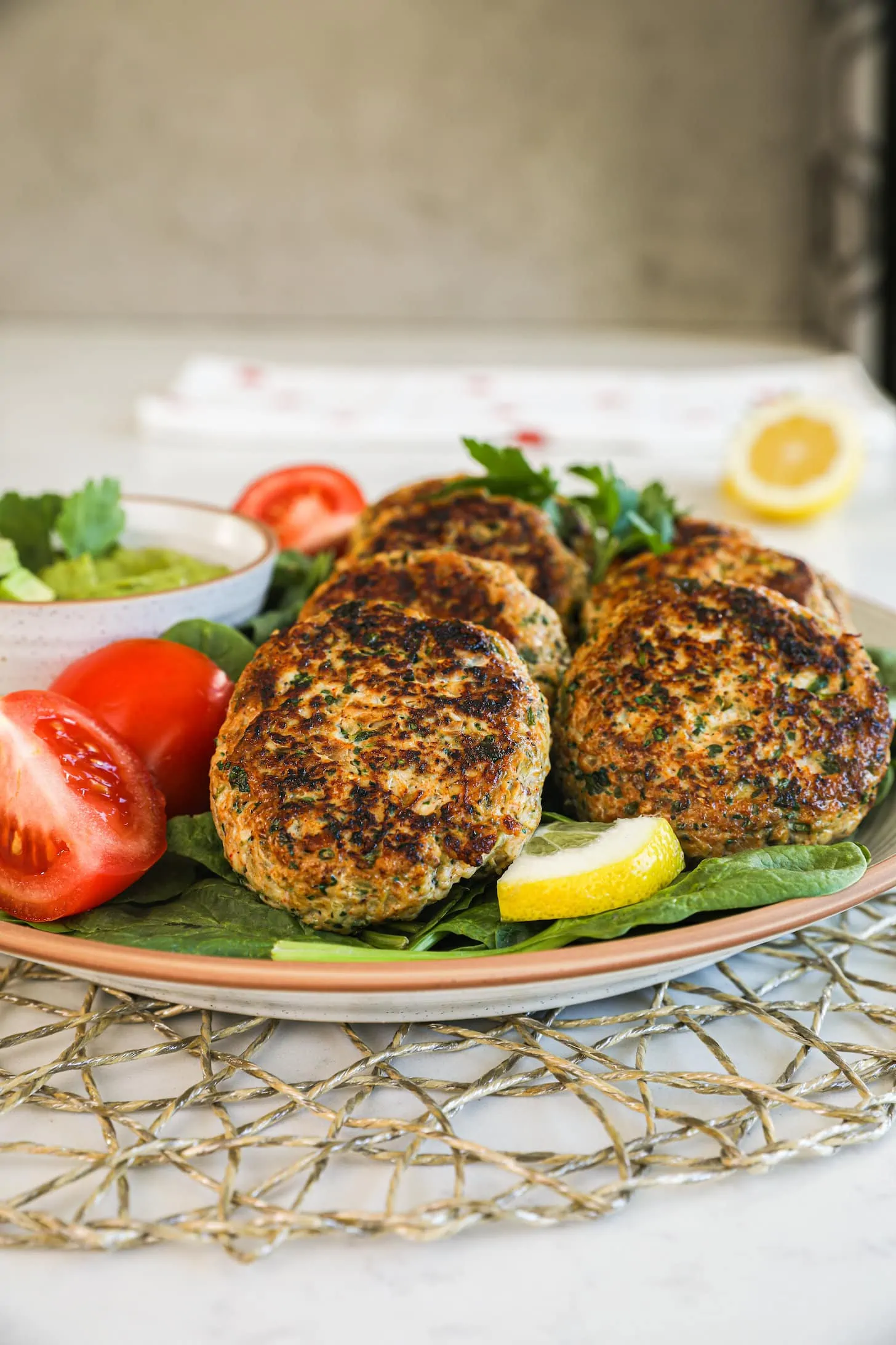 a plate of cooked patties overlaid on one another on a bed of greens with a bowl of dip on the side - perspective shot.
