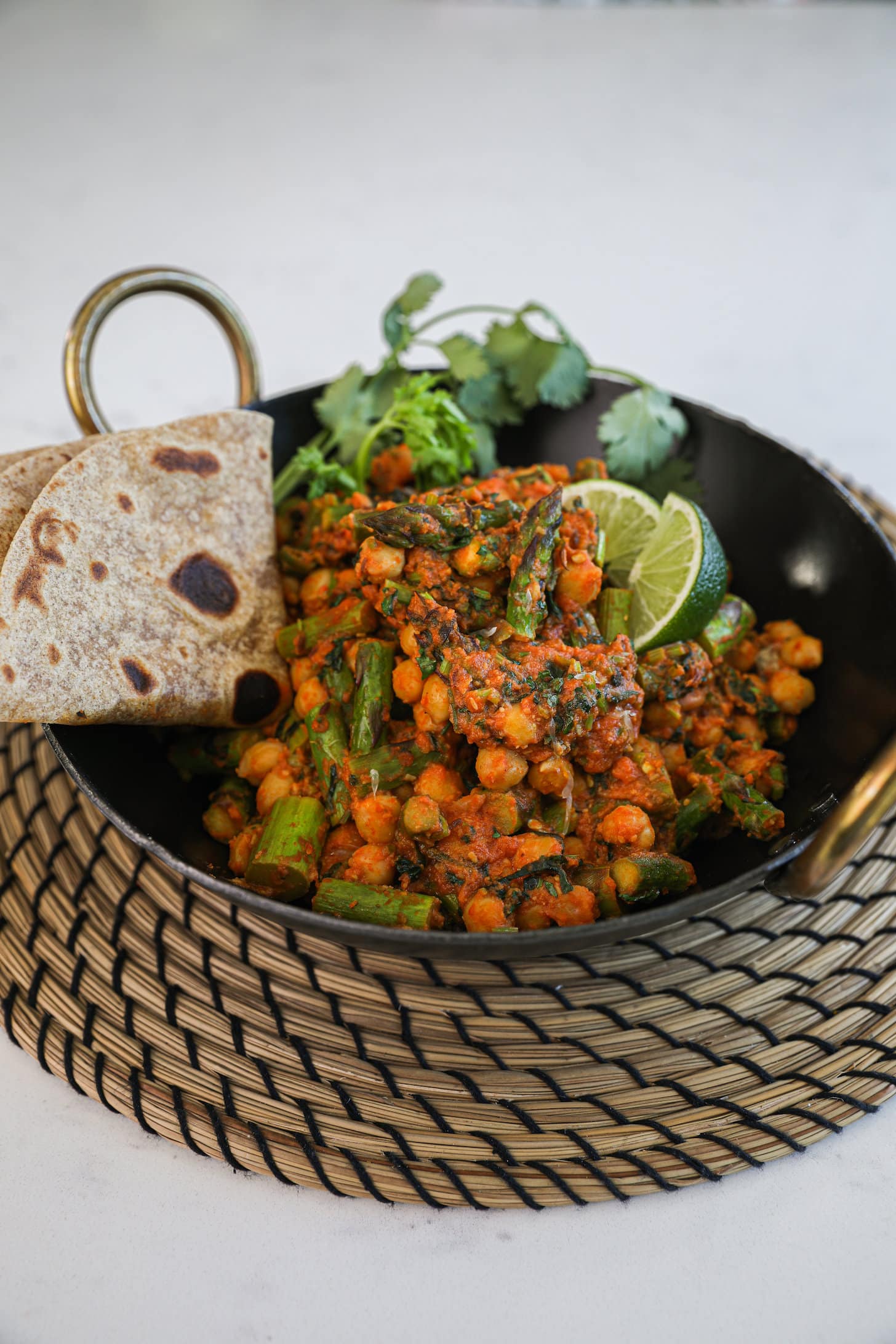 a wok filled with cooked chickpeas and asparagus in a orange/red sauce with a side of folded chapati.
