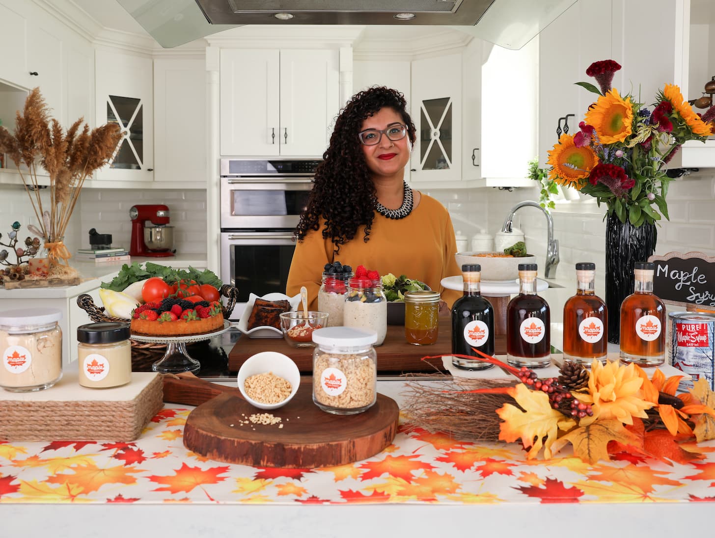 a lady behind her kitchen counter with a display of maple syrup products.