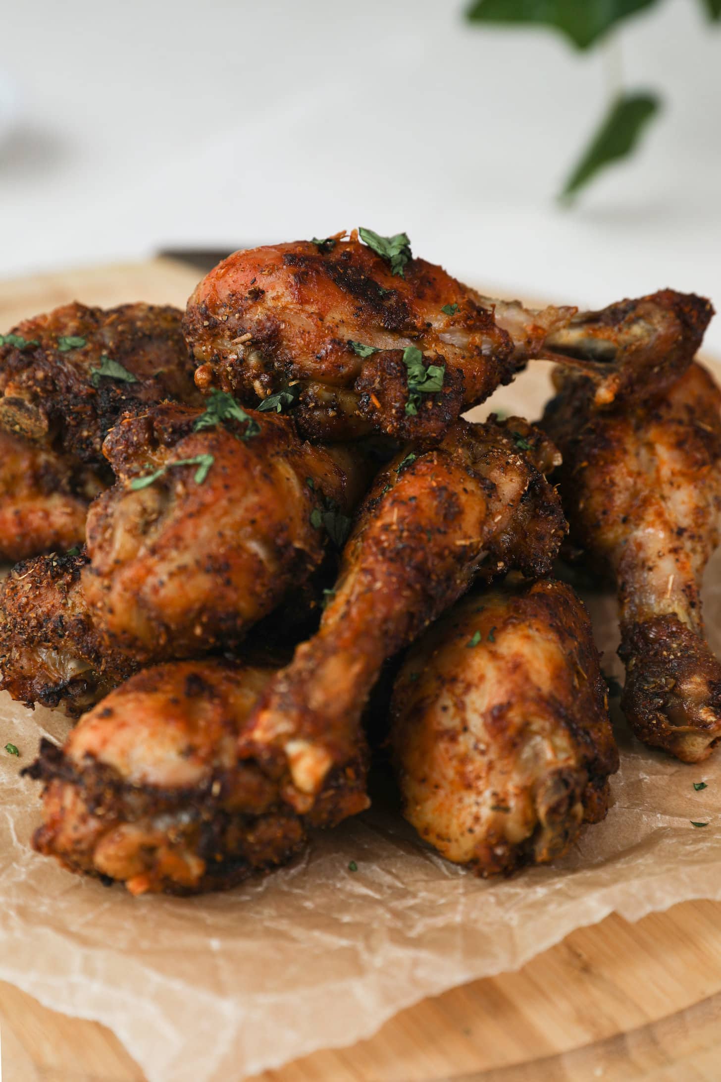 a perspective image of a pile of cooked chicken drumsticks topped with chopped herb.