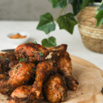 a pile of chicken drumsticks on a board with a plant in the background.