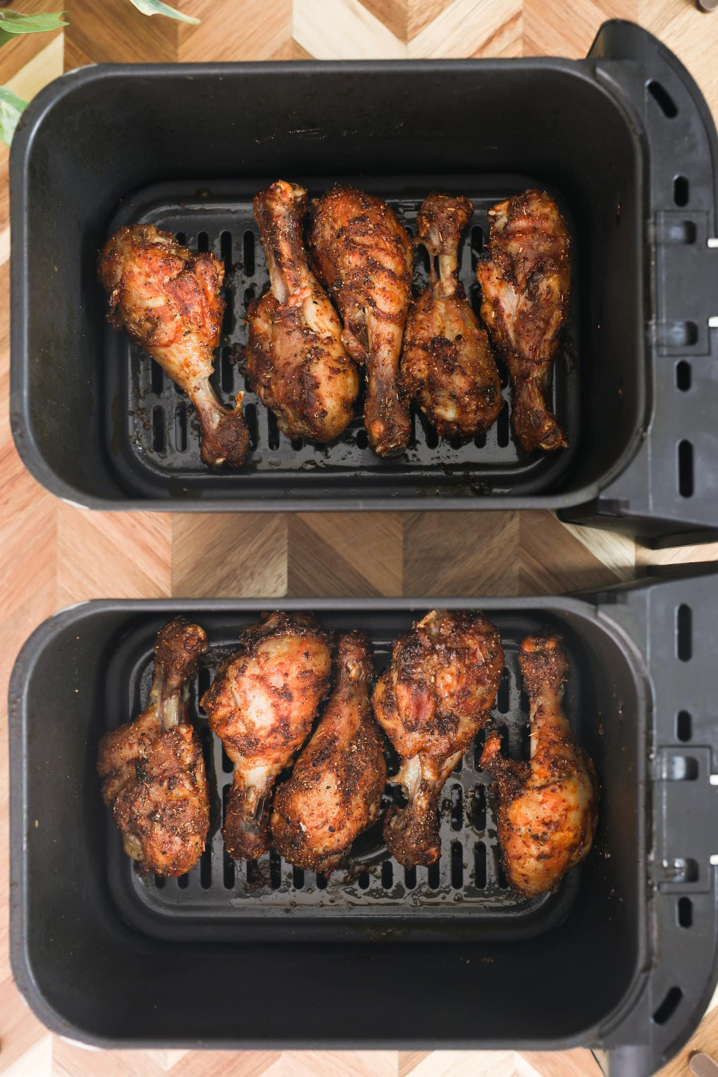 overhead image of cooked chicken drumsticks in air fryer baskets.