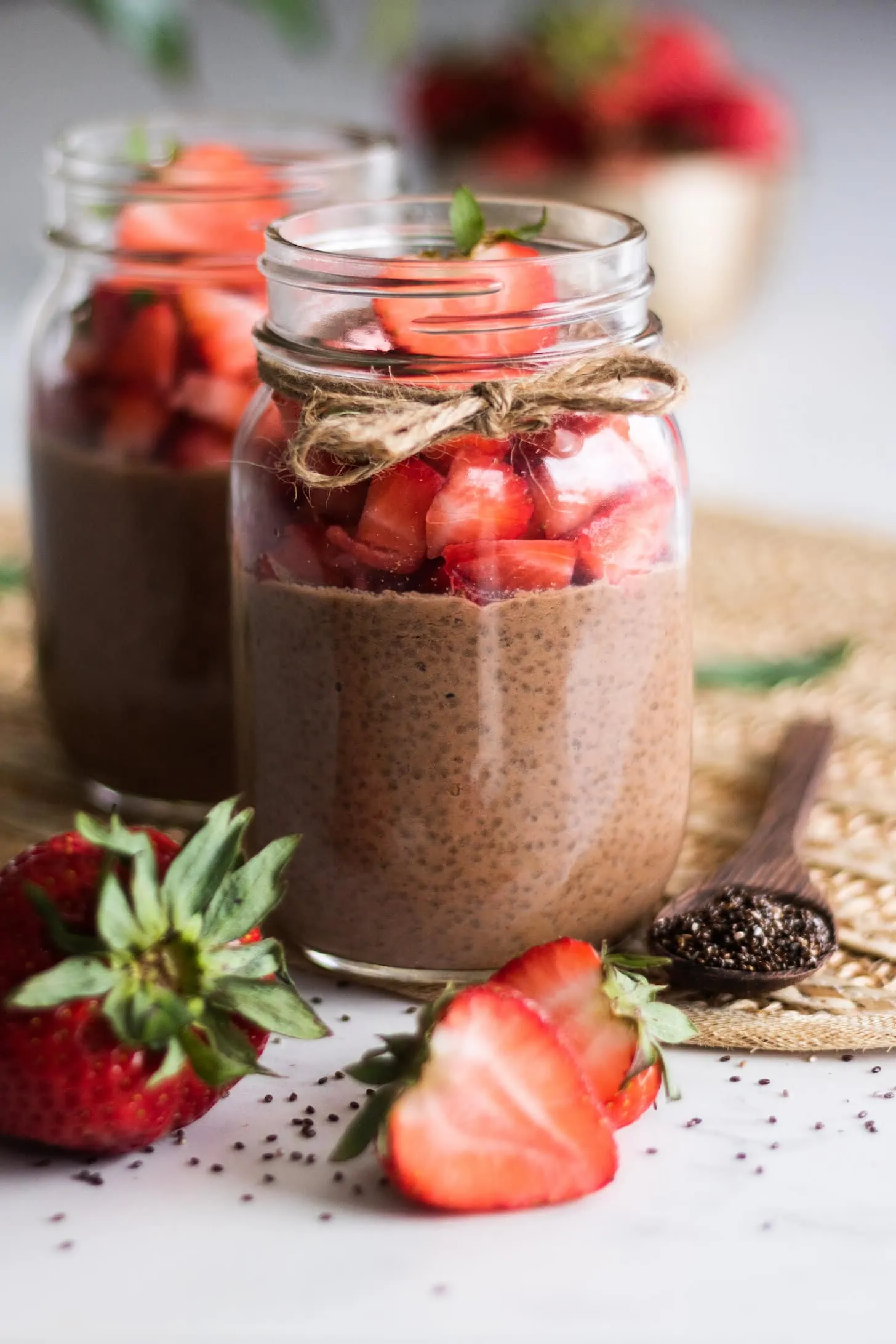 mason jars of chocolate chia pudding topped with chopped strawberries with fresh strawberries in the foreground.