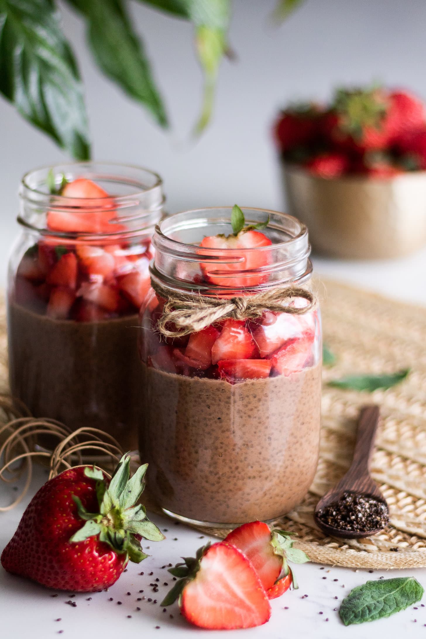 mason jars of chocolate chia pudding topped with chopped strawberries with a bowl of strawberries in the background.